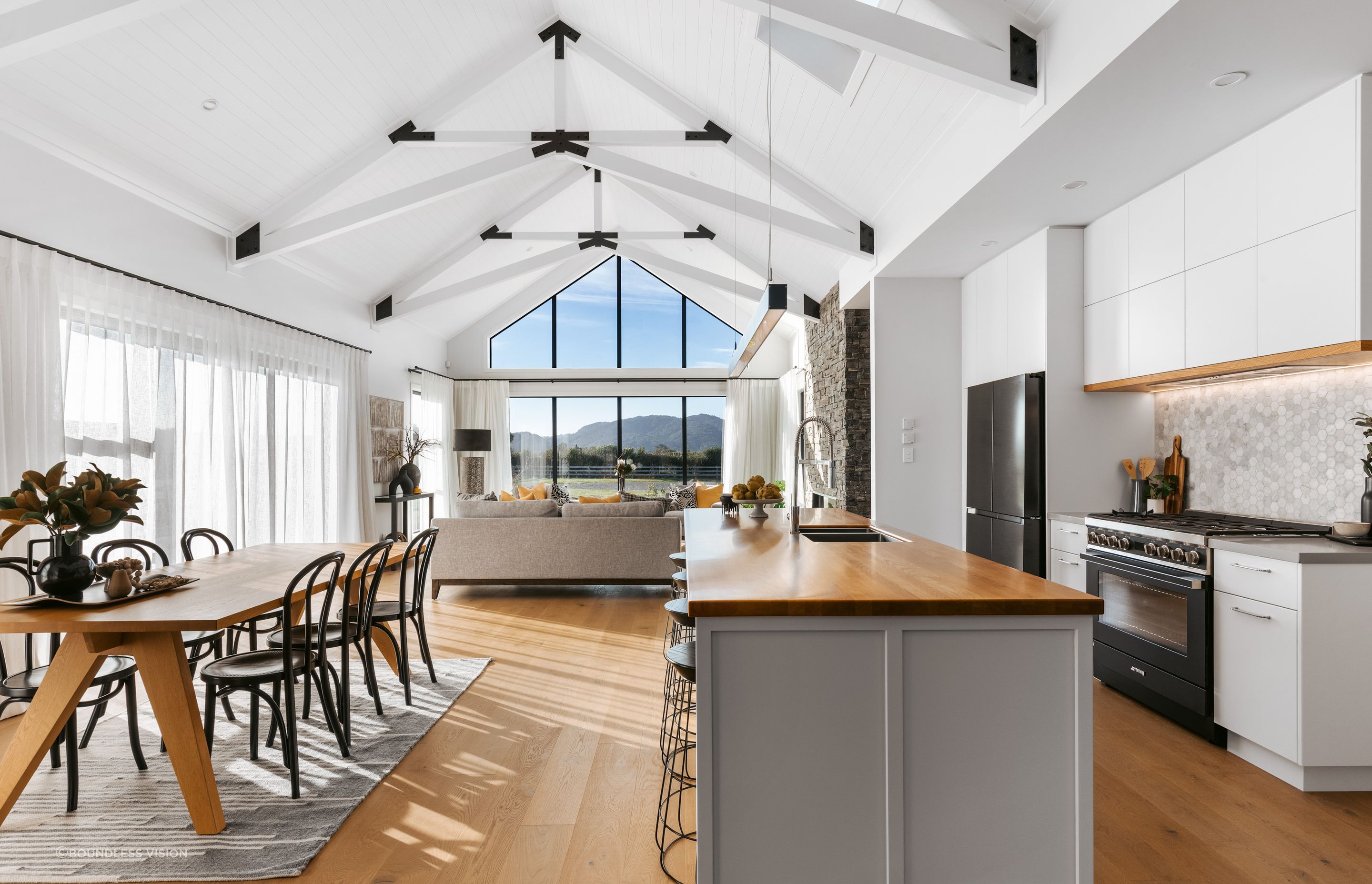 The open-plan living wing is a bright, voluminous space, with full-height windows extending up towards the raked ceilings.