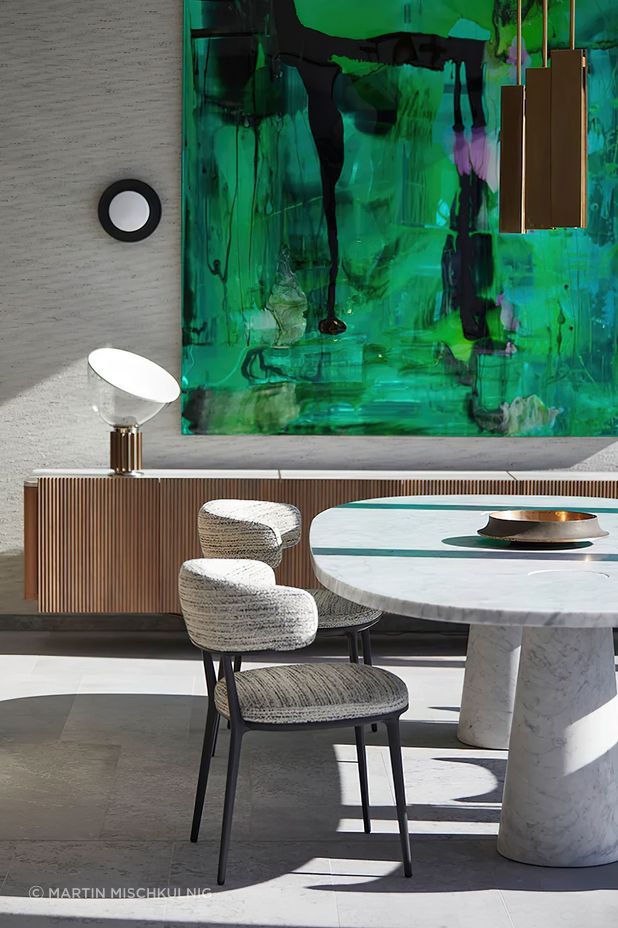 Against the backdrop of a vibrant green Dale Frank painting and Sydney Harbour, the Agape Casa dining table designed by Angelo Mangiarotti in cool grey Carrara marble, the Caratos upholstered dining chairs designed by Antonio Citterio for Maxalto, the iconic Taccia table lamp designed by Giacomo and Achille Castiglioni for Flos, the Bell Sconce wall light designed by Post Company for Roll & Hill, and the Charlotte low cabinet designed by Carlo Colombo for Giorgetti. Photo © Martin Mischkulnig