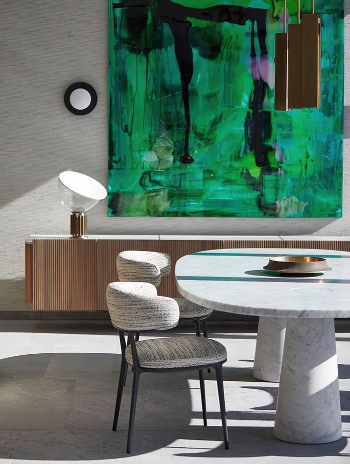 Against the backdrop of a vibrant green Dale Frank painting and Sydney Harbour, the Agape Casa dining table designed by Angelo Mangiarotti in cool grey Carrara marble, the Caratos upholstered dining chairs designed by Antonio Citterio for Maxalto, the iconic Taccia table lamp designed by Giacomo and Achille Castiglioni for Flos, the Bell Sconce wall light designed by Post Company for Roll & Hill, and the Charlotte low cabinet designed by Carlo Colombo for Giorgetti. Photo © Martin Mischkulnig