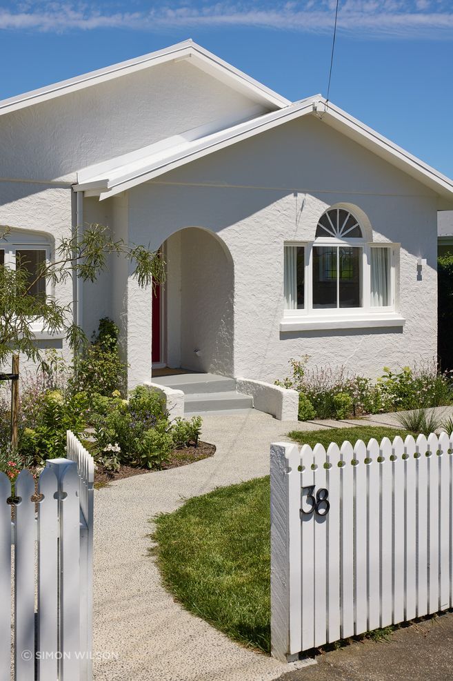 Pop-Up Book retains the original stucco bungalow’s character at the street, framed by a traditional picket fence and cottage garden.