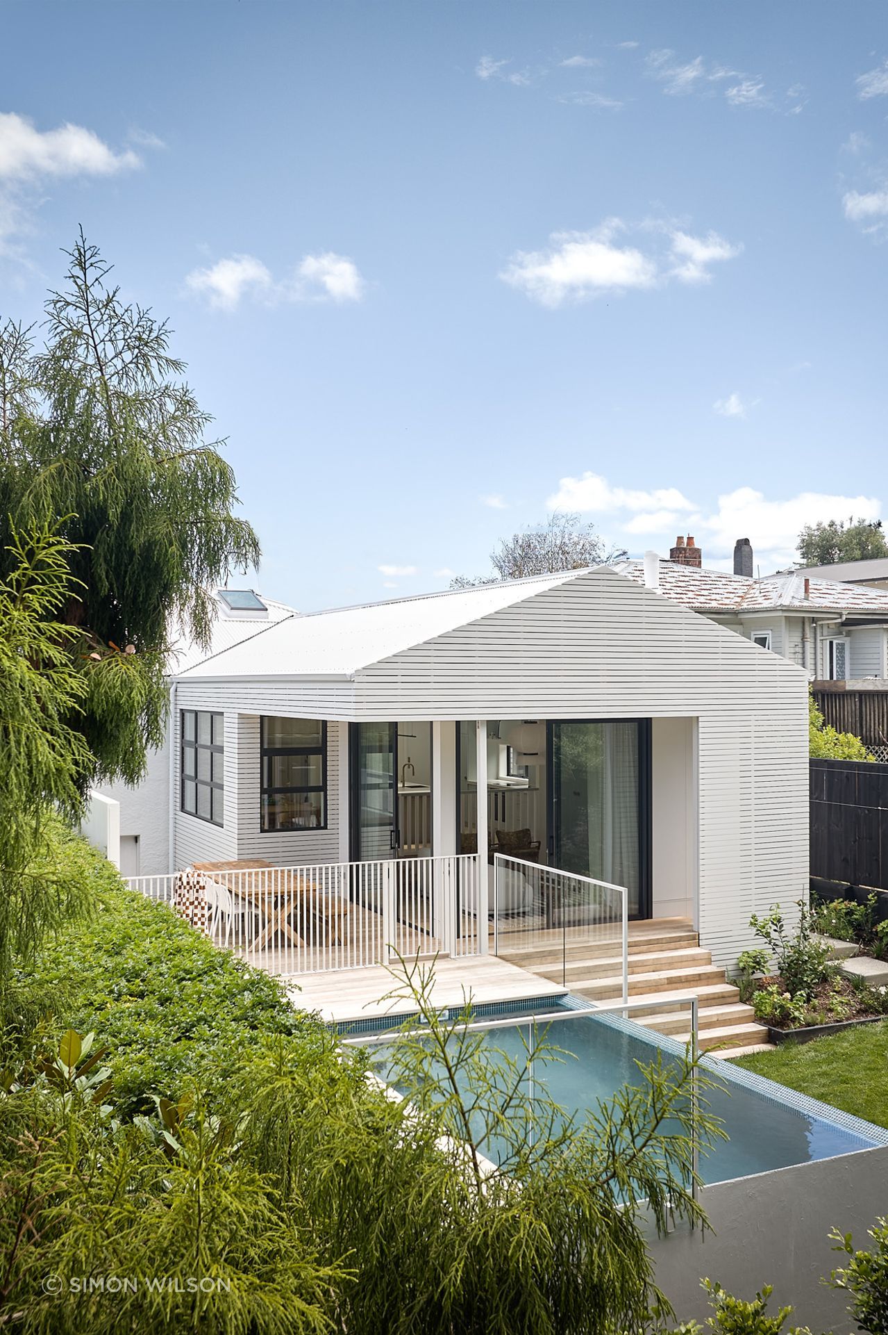 At the rear, a contemporary extension steps with the sloping site, connecting the new living spaces to the pool and garden.
