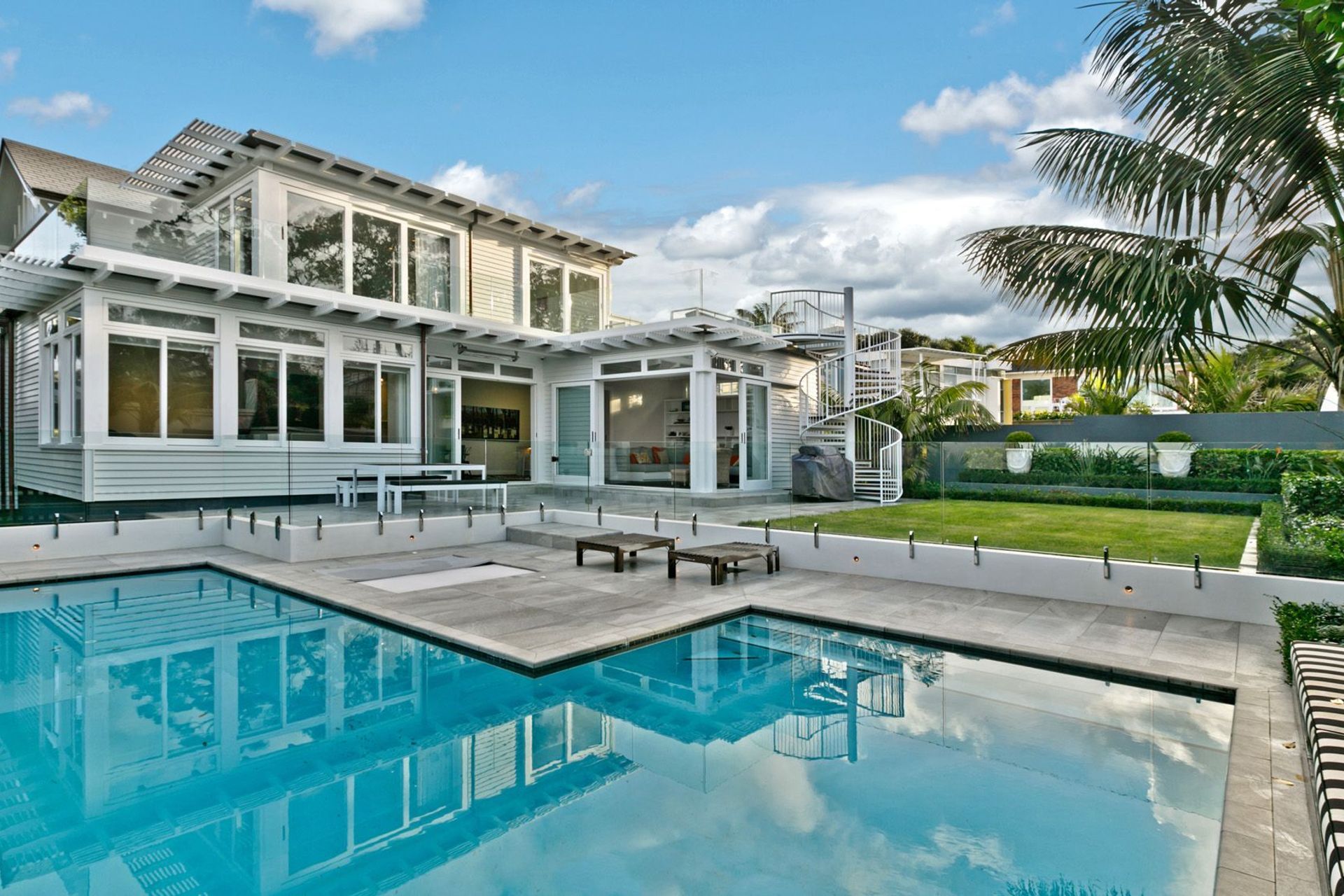 An L-shaped swimming pool seamlessly occupies the garden corner of this stylish home in Takapuna.