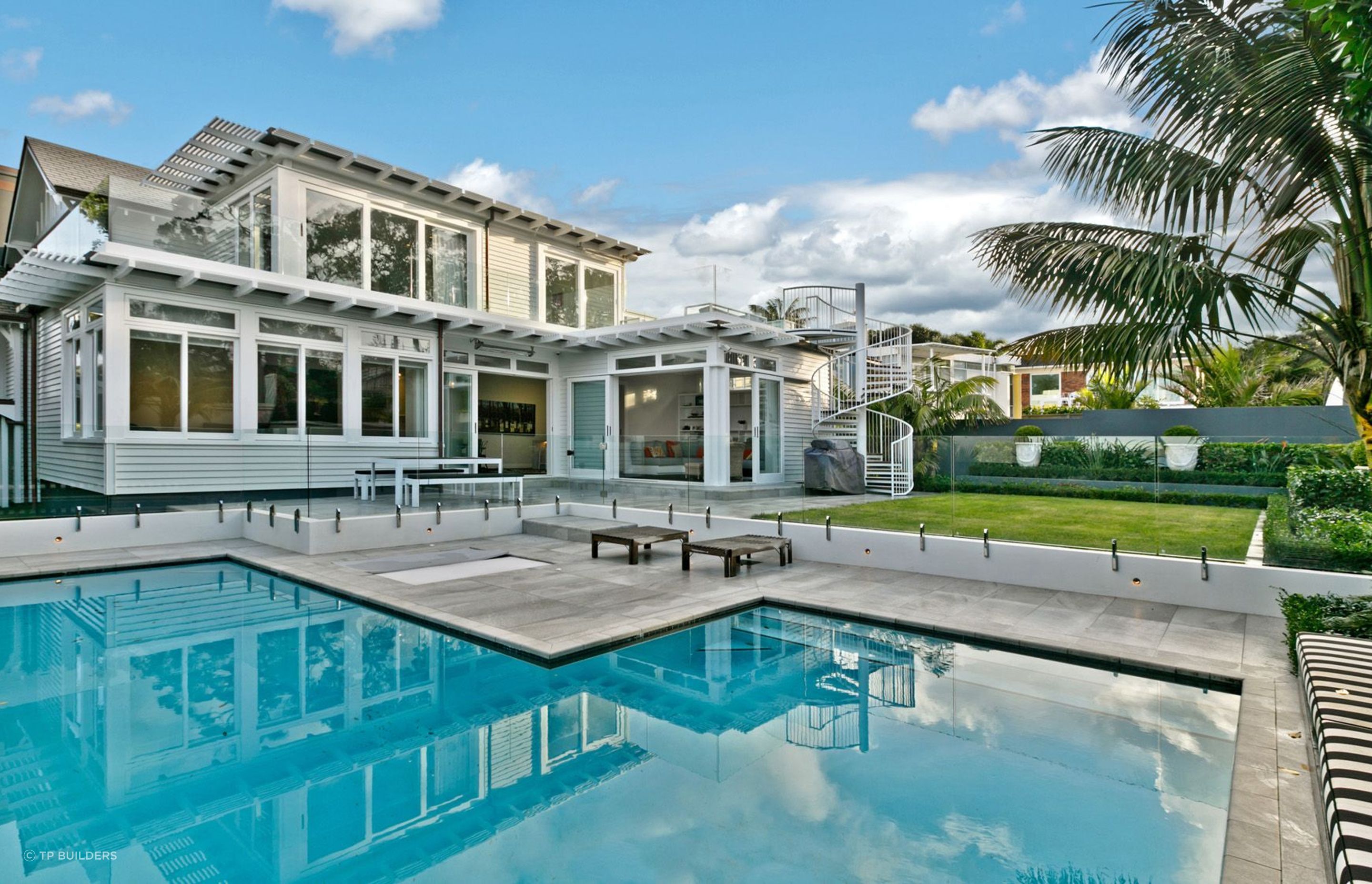 An L-shaped swimming pool seamlessly occupies the garden corner of this stylish home in Takapuna.