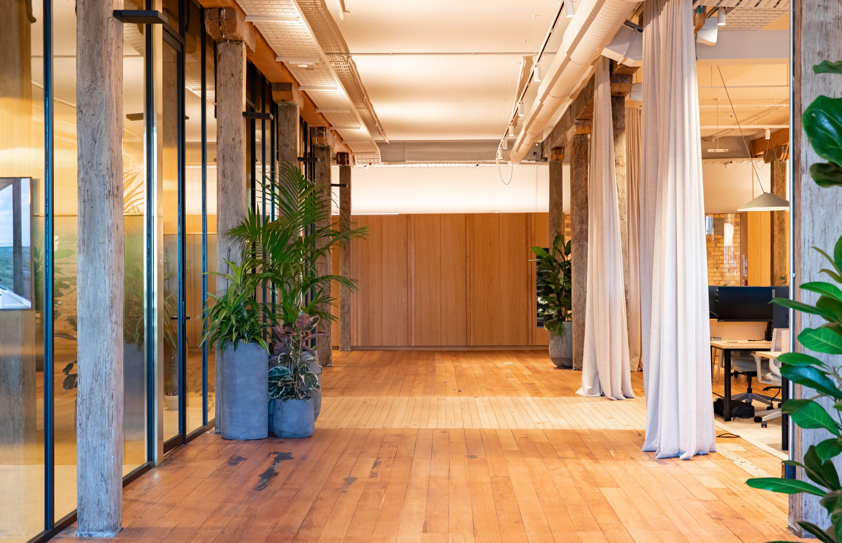 Meeting rooms are pictured to the left, with workstations across the walkway. | Photographers: Oliver Compton &amp; Millie Cossou