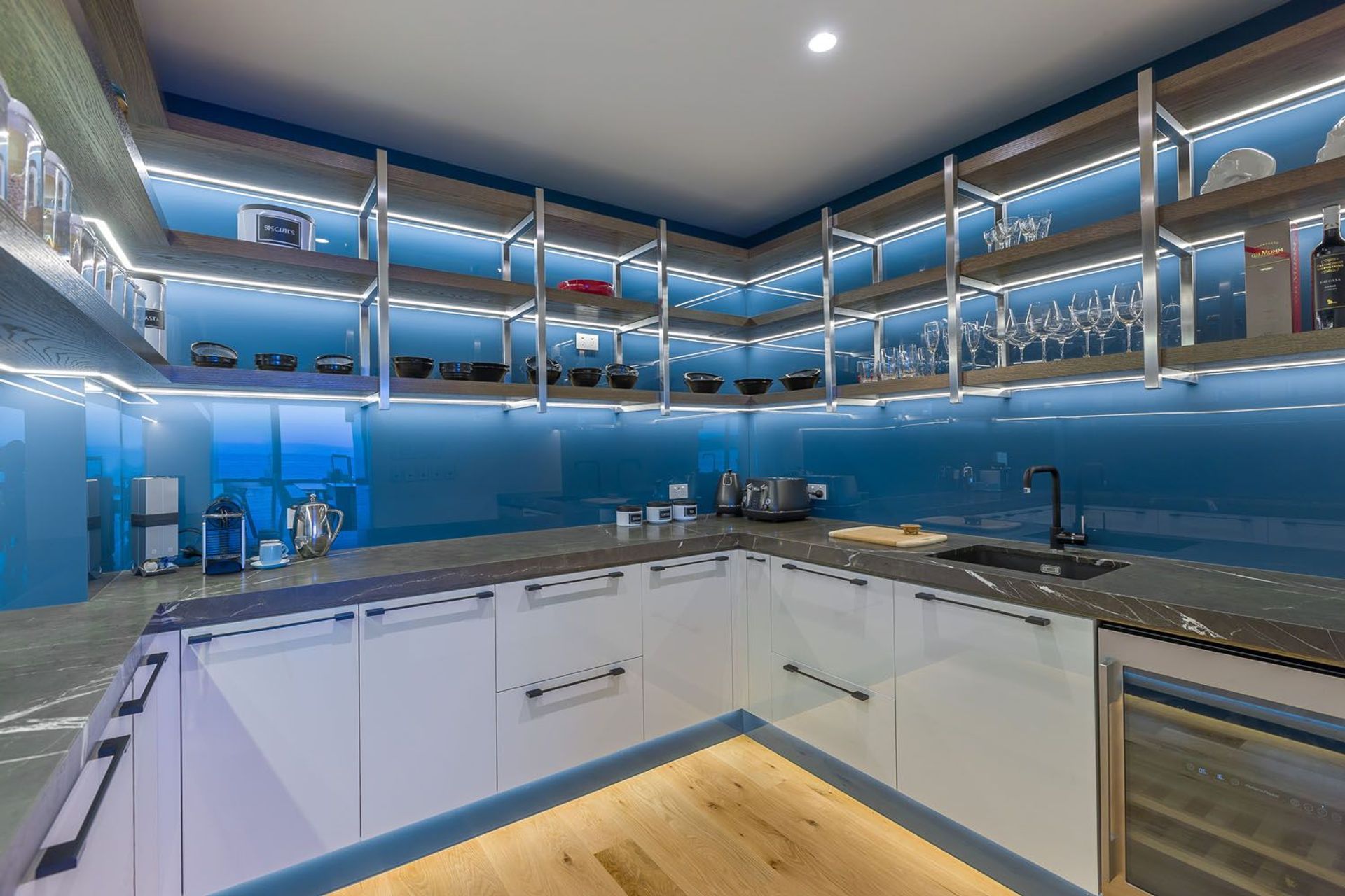 This stunning kitchen designed by Mal Corboy features glass toe-kicks that are up-lit with LED lighting, creating a striking lighting effect against the blue coloured glass. Image credit: Kallan MacLeod.