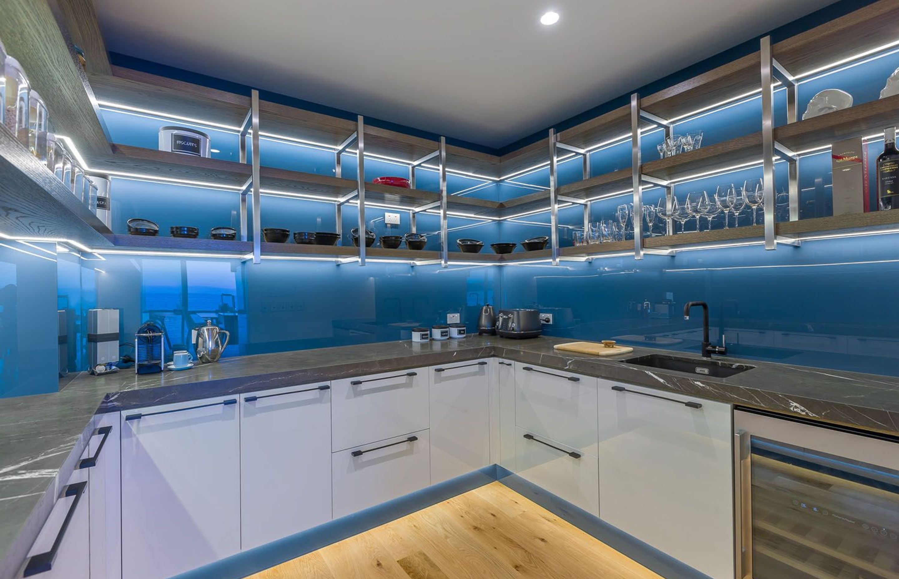 This stunning kitchen designed by Mal Corboy features glass toe-kicks that are up-lit with LED lighting, creating a striking lighting effect against the blue coloured glass. Image credit: Kallan MacLeod.