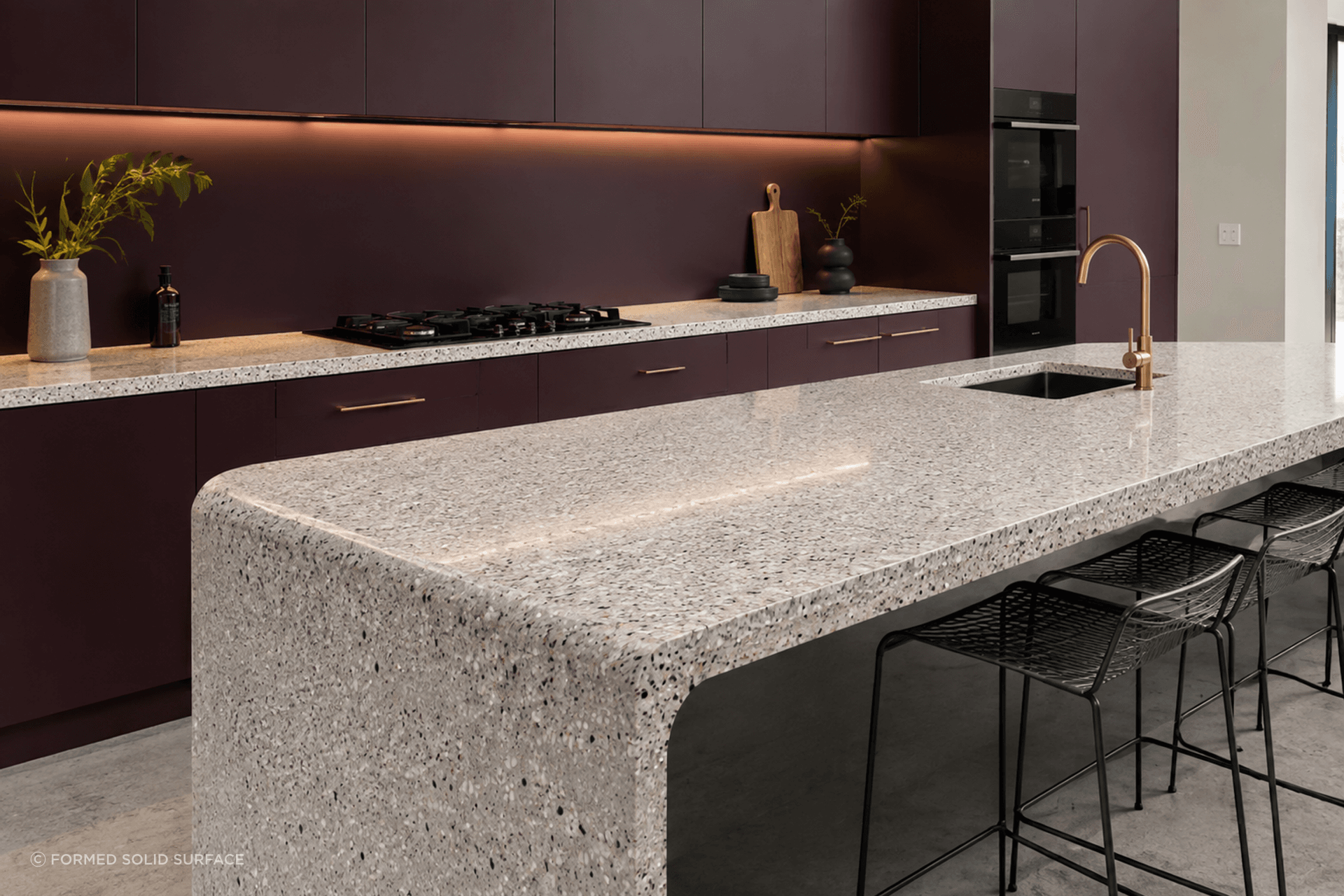 A statement in seamless form. Thermoformed solid surface creates a beautifully curved waterfall island, bringing softness and sculptural detail to this contemporary kitchen while contrasting against rich eggplant cabinetry.