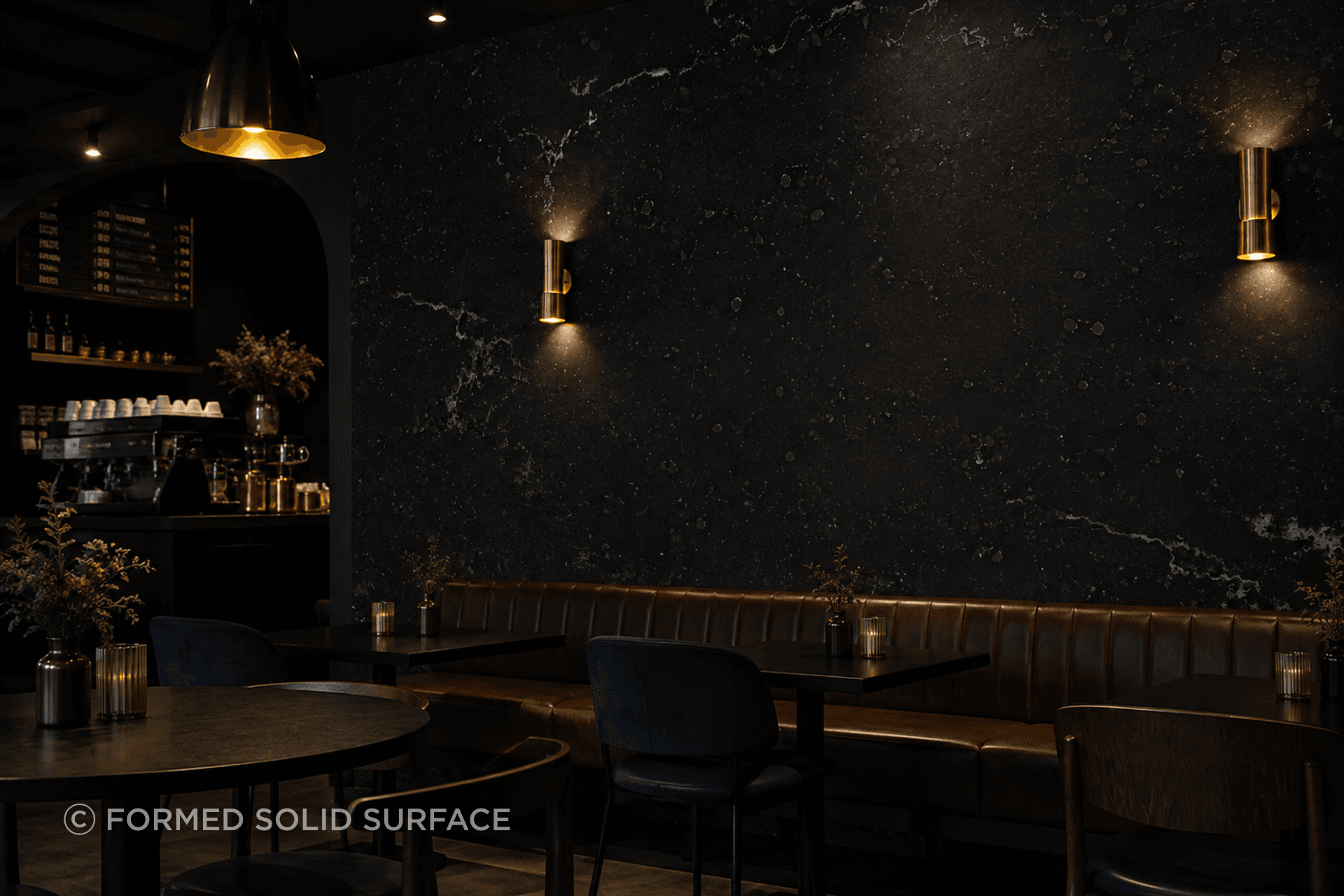 Material can define the mood of a space. Dark solid surface wall cladding creates a dramatic architectural backdrop, complemented by warm brass lighting, chocolate leather and deep navy accents for a refined hospitality interior.
