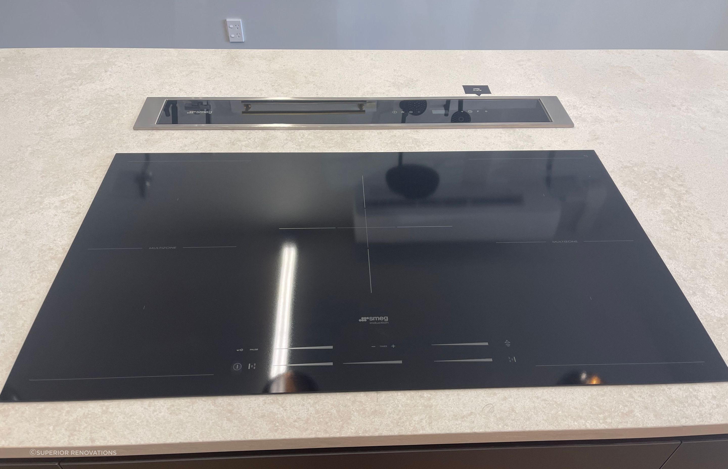 Large induction stovetop from SMEG with a safety feature in our kitchen showroom in Auckland. The downdraft range hood goes back into the benchtop when not in use.