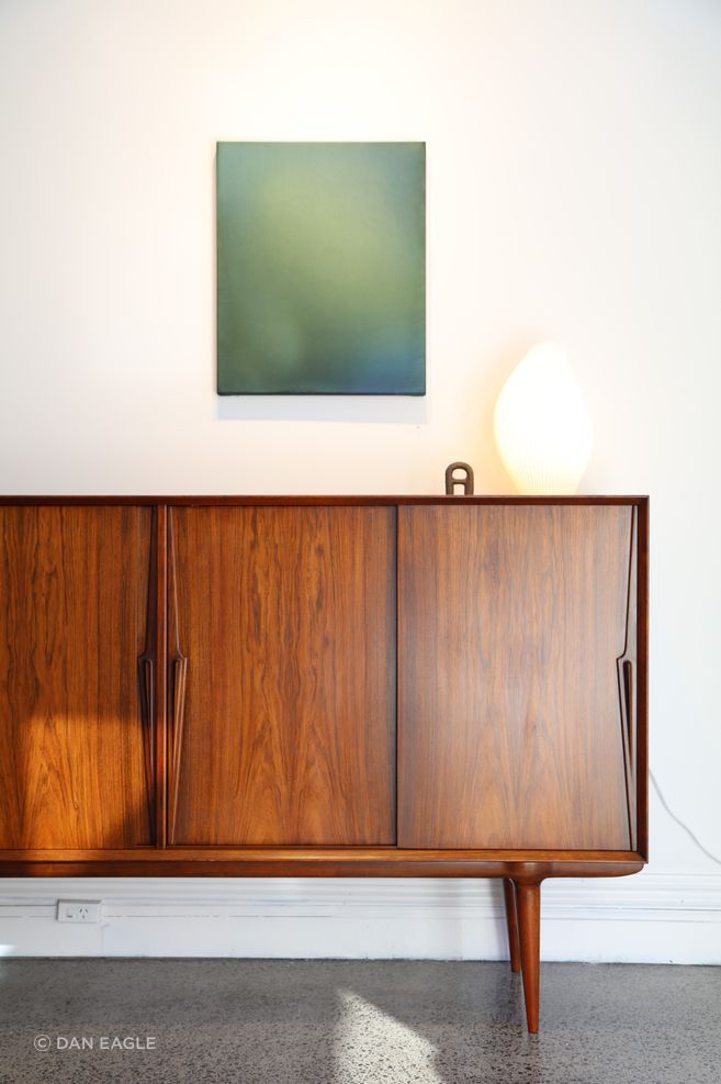 Artwork by Kate Serebrianskaia With Eyes Wide Open, 2026. Acrylic fluid and ink on canvas.
Vintage Omann Jun Rosewood Sideboard from Mr. Bigglesworthy at Good Form, Romy Table Lamp by Cam Barrett from Good Form, Bokk Bottle Opener by Nedre Foss from Good Form.