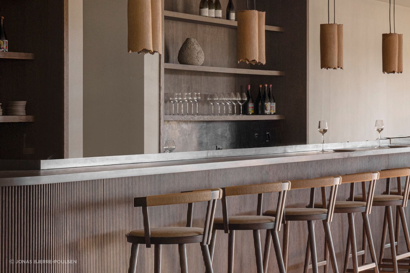 The bar pairs dark timber, woven details and warm natural light. Photography by Jonas Bjerre-Poulsen.