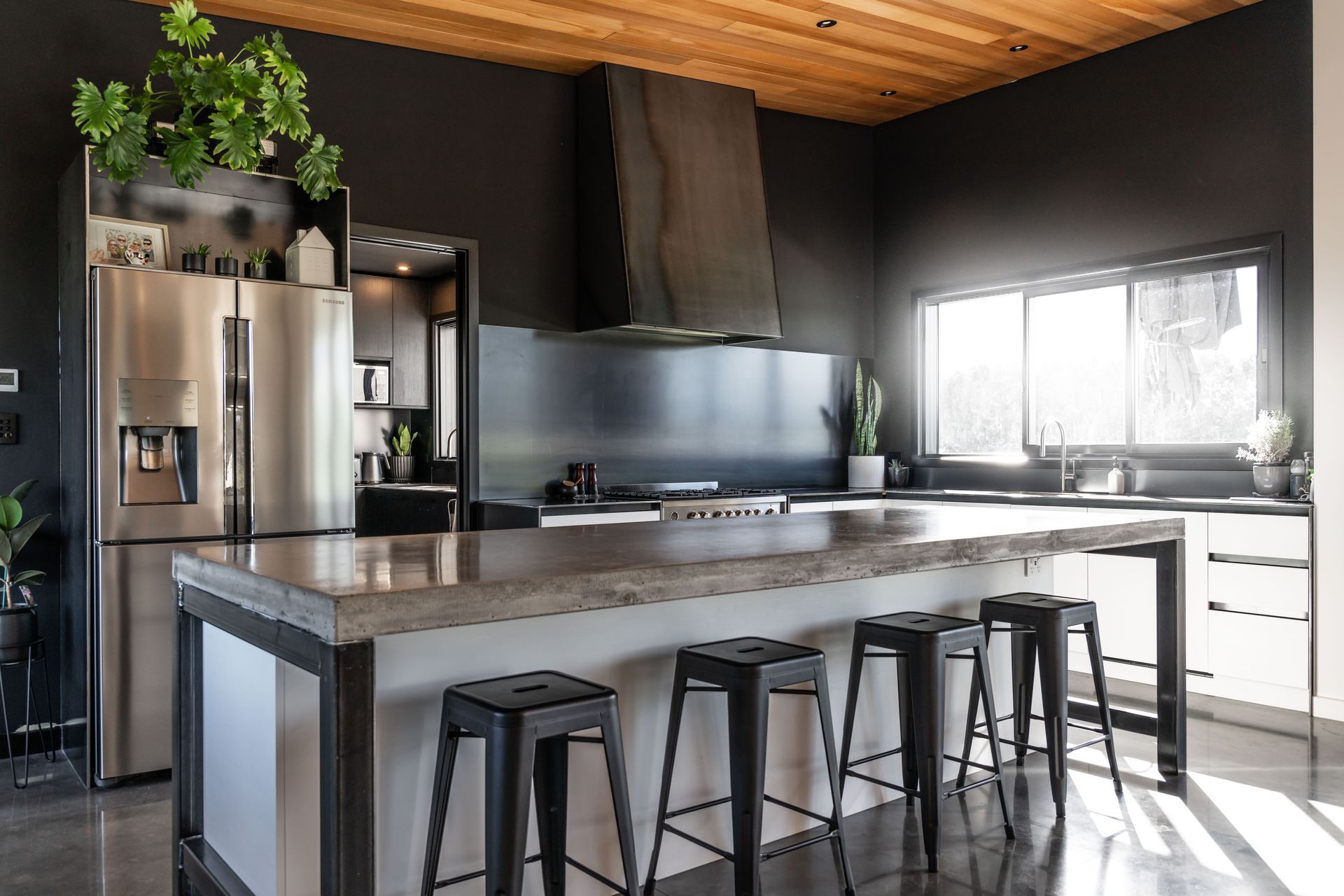 Black walls and a warm timber-clad ceiling create drama in this intustrial-esque kicthen.