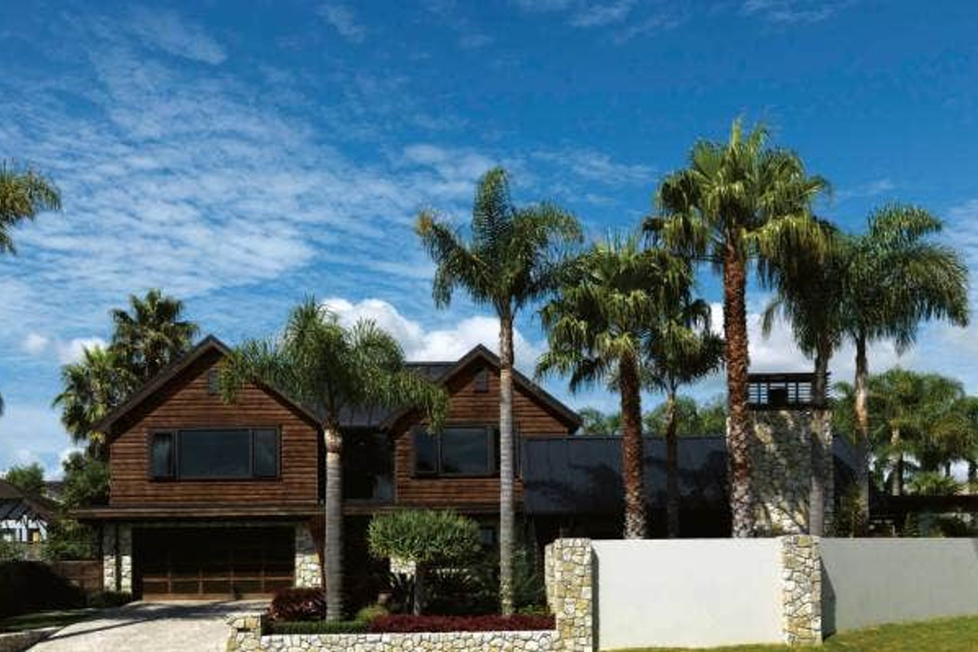 Existing palms add a mature touch to the garden while cedar cladding and Te Kuiti limestone were chosen for their natural earthy feel; the driveway was resurfaced using pebble-covered sheets from Island Stone.
