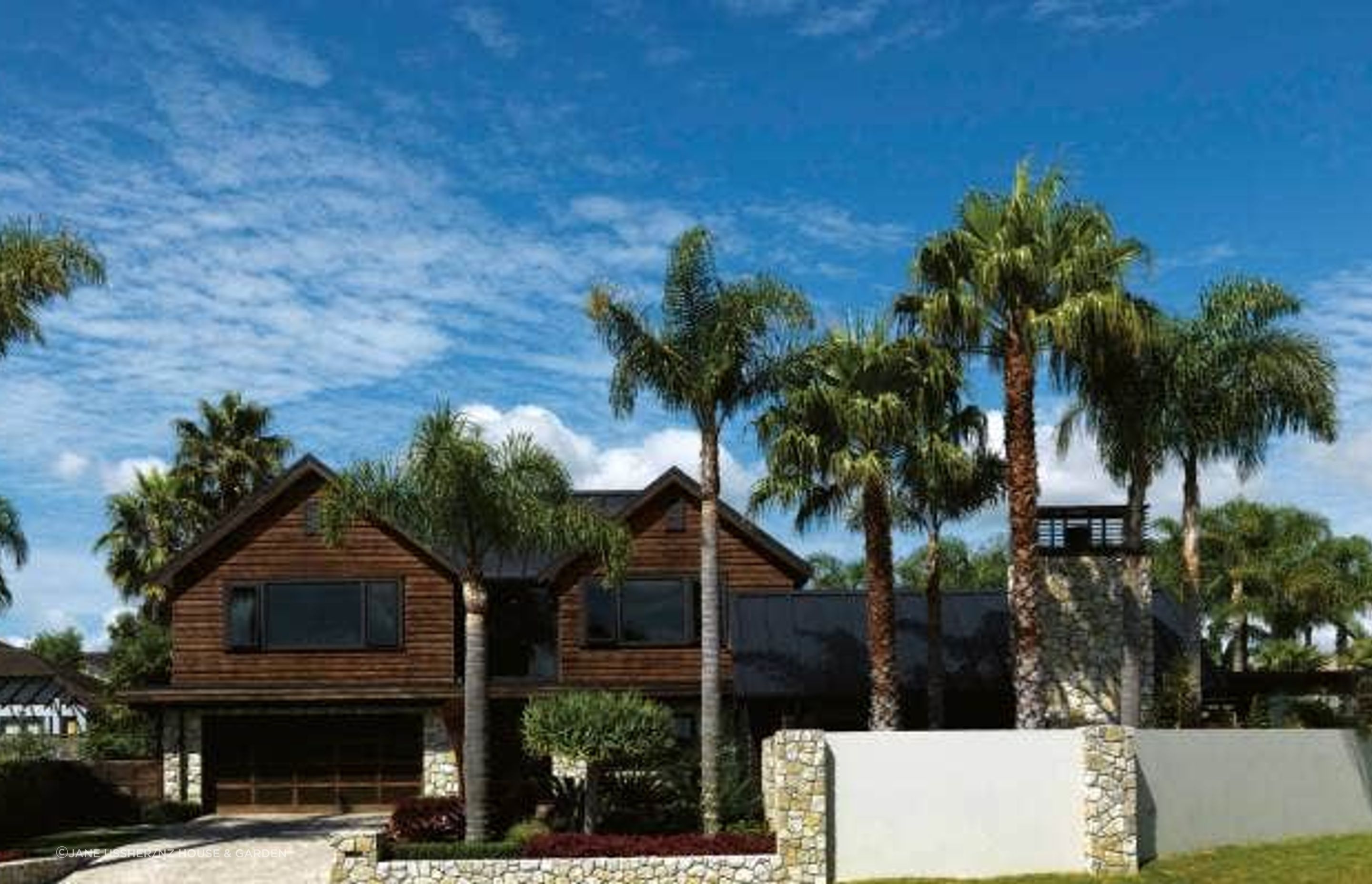 Existing palms add a mature touch to the garden while cedar cladding and Te Kuiti limestone were chosen for their natural earthy feel; the driveway was resurfaced using pebble-covered sheets from Island Stone.