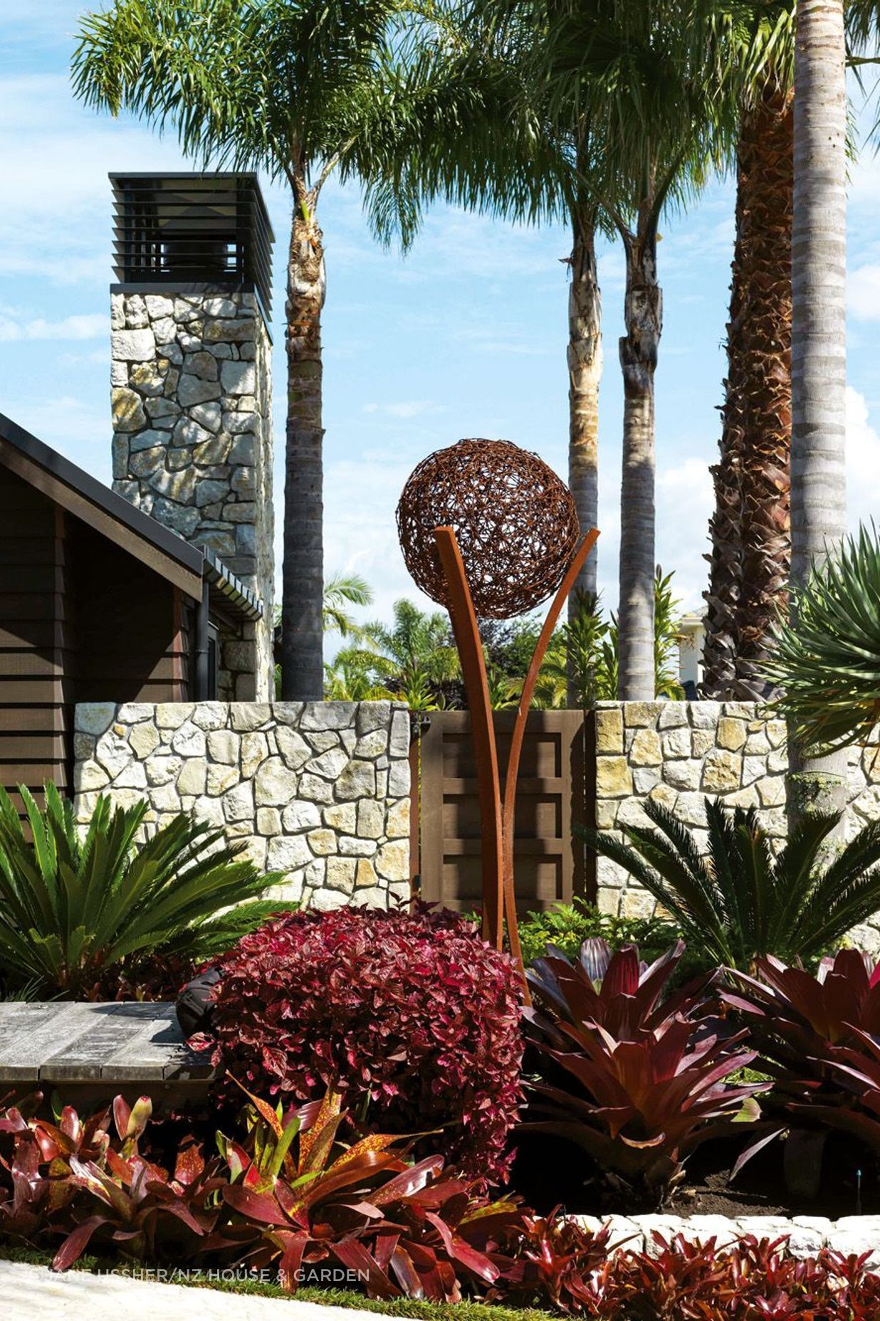 A boardwalk adds to the resort-like feel of the entrance, with planting that includes cycads, iresine and bromeliads; the sculpture is by Wire Art – the couple spotted a similar one at a Wānaka vineyard.