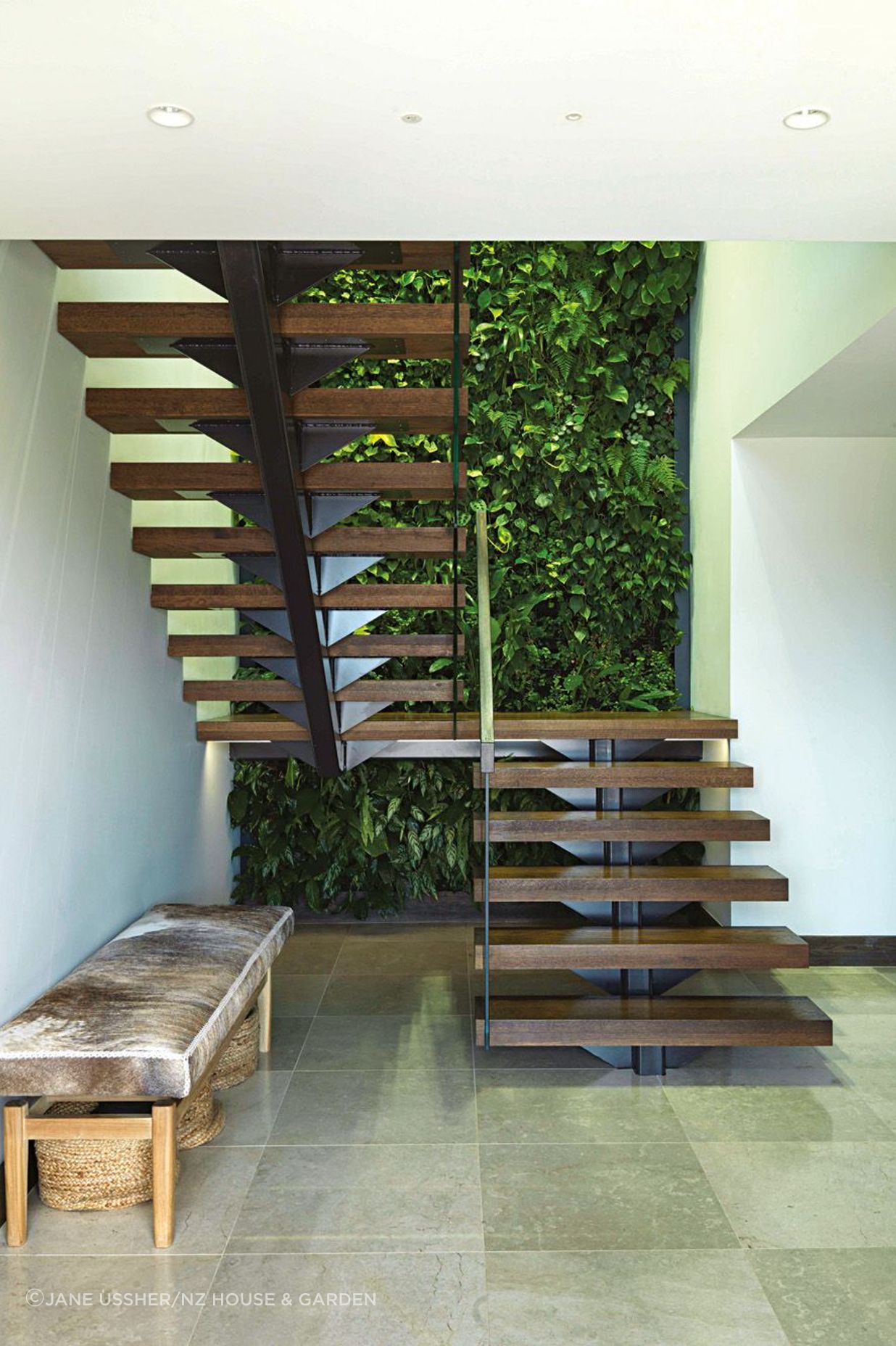 The floating stairs give an airy feel to the stairwell; the McNalls have chosen earthy, natural materials like the cowhide-covered bench and the ivory cross-cut limestone tiles used inside and out.