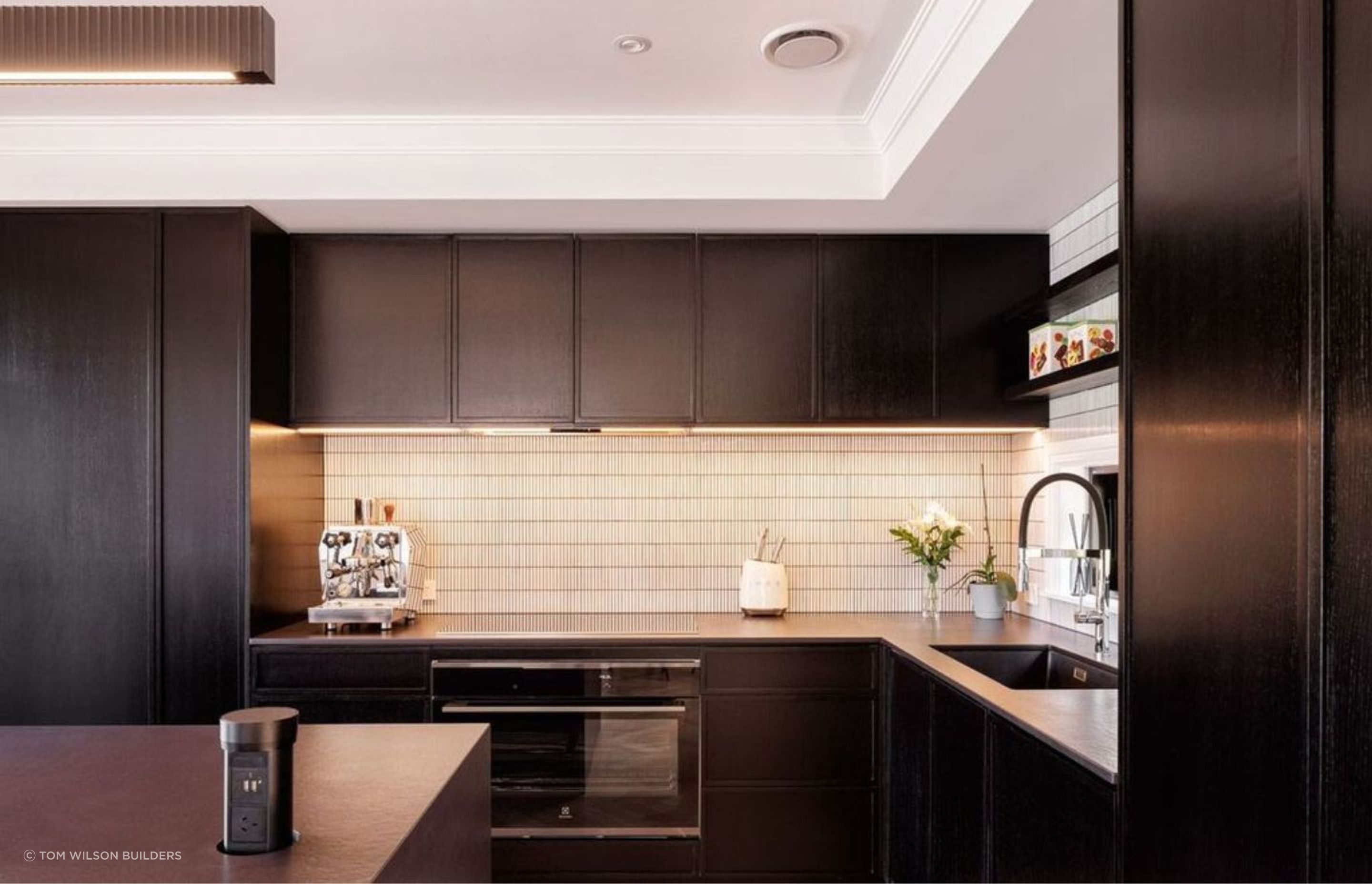 The kitchen, also known as the heart of the home, is designed with dark stained wooden cabinets, sublty lightened with white tiling to add texture and contrast