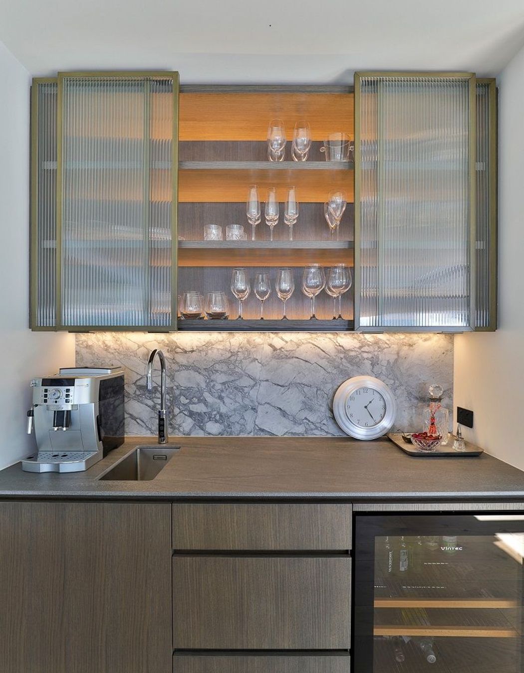 This narrow-reeded glass cabinetry by Hewe Architectural Cabinetry elevates this bar and subtly conceals the items within.