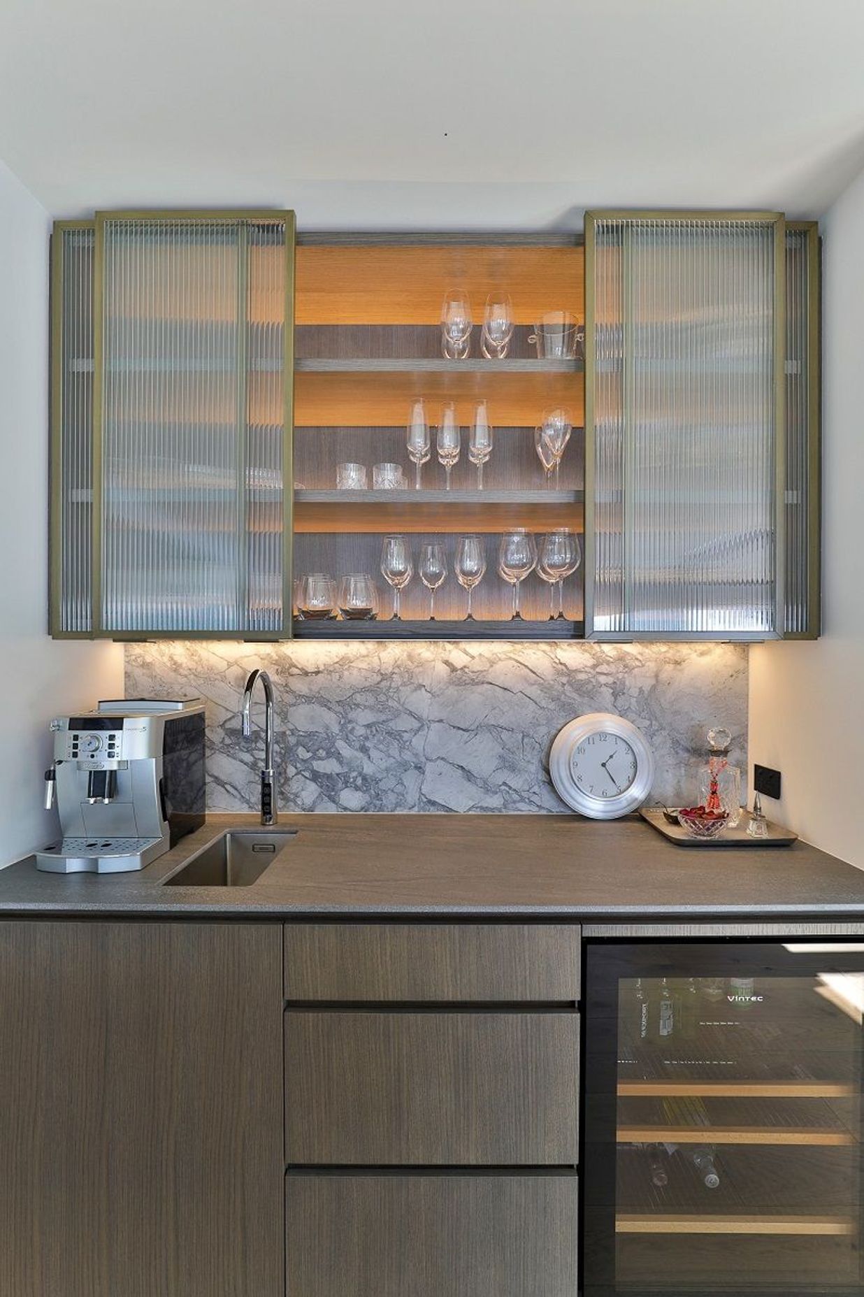 This narrow-reeded glass cabinetry by Hewe Architectural Cabinetry elevates this bar and subtly conceals the items within.