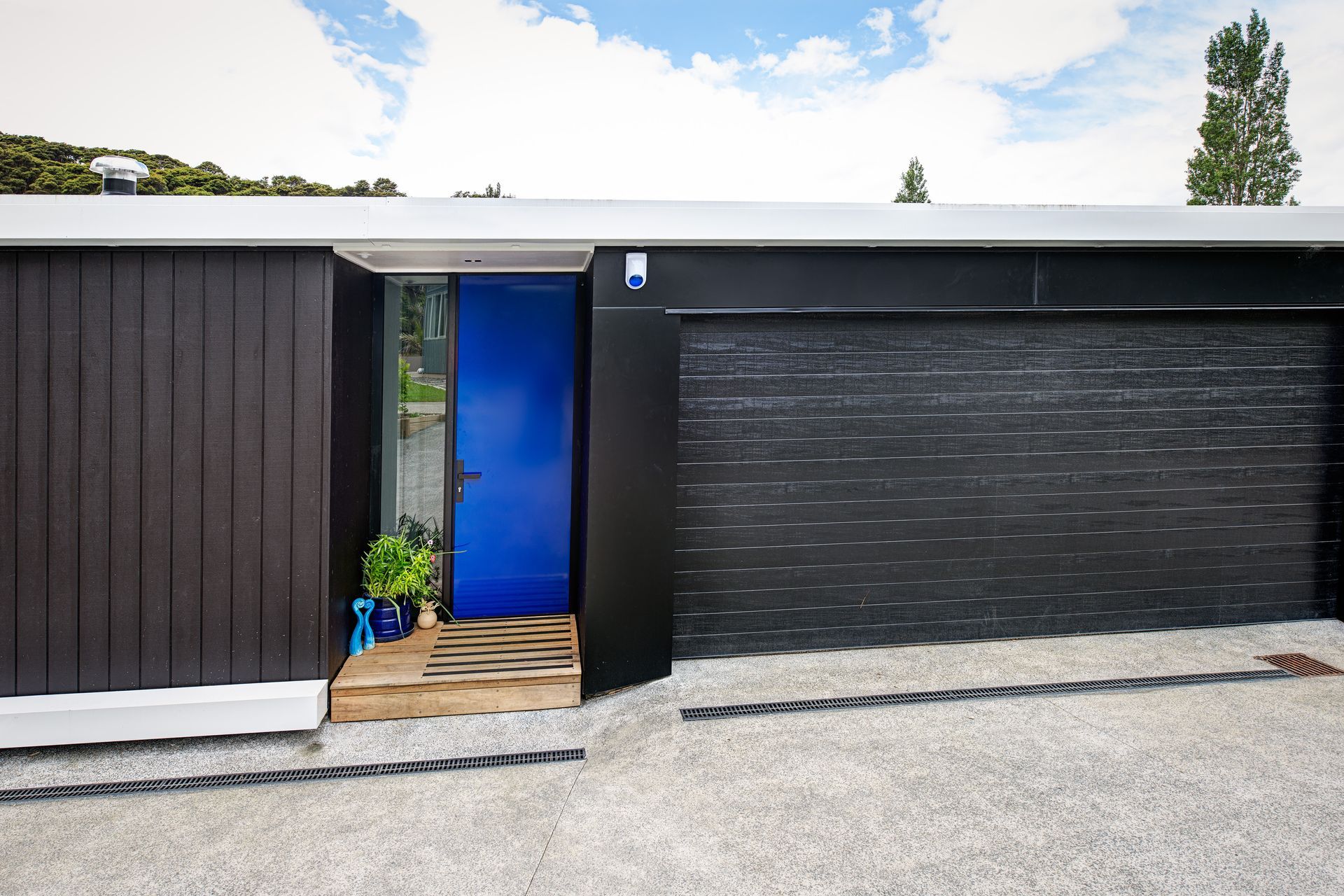 A vibrant blue Plasma Glass Entrance Door is matched with a pot plant, sculpture and even the security system