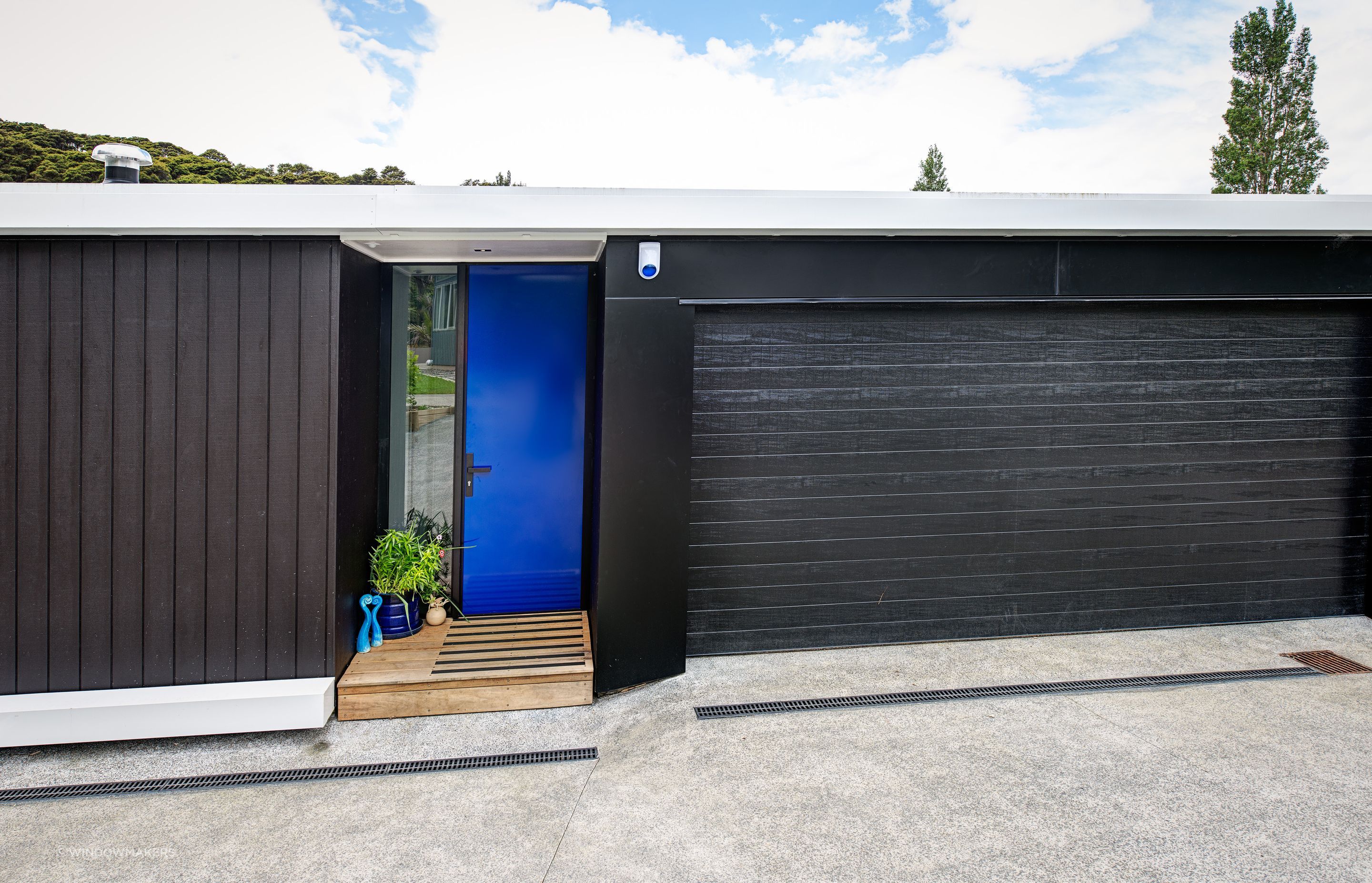 A vibrant blue Plasma Glass Entrance Door is matched with a pot plant, sculpture and even the security system