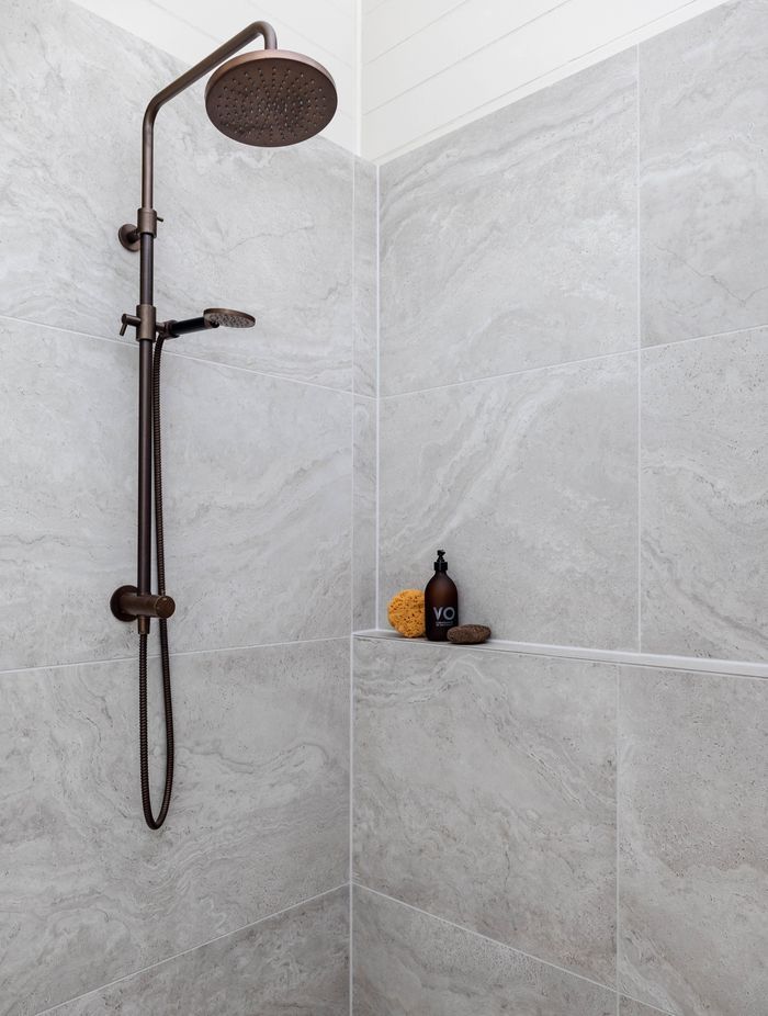 The Plumbline Shower Buddy Column in 'Aged Brass' contrasts with the textural tiles from Quantum.