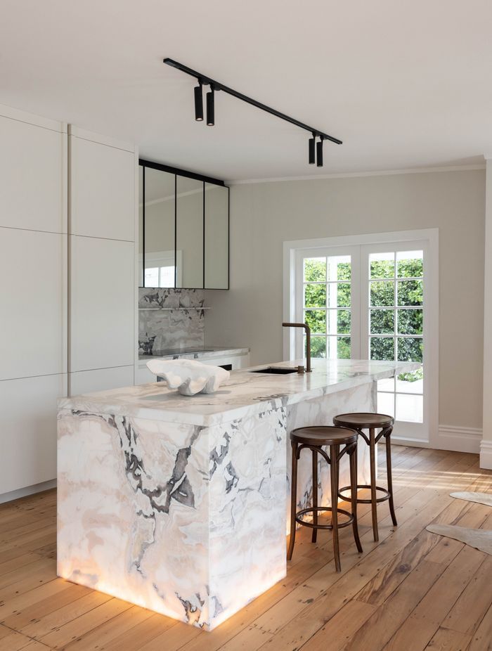 Lighting within the base of the island bench brings warmth to the space. Above, a track light from Coombes + Gabbie provides excellent task lighting for food preparation.