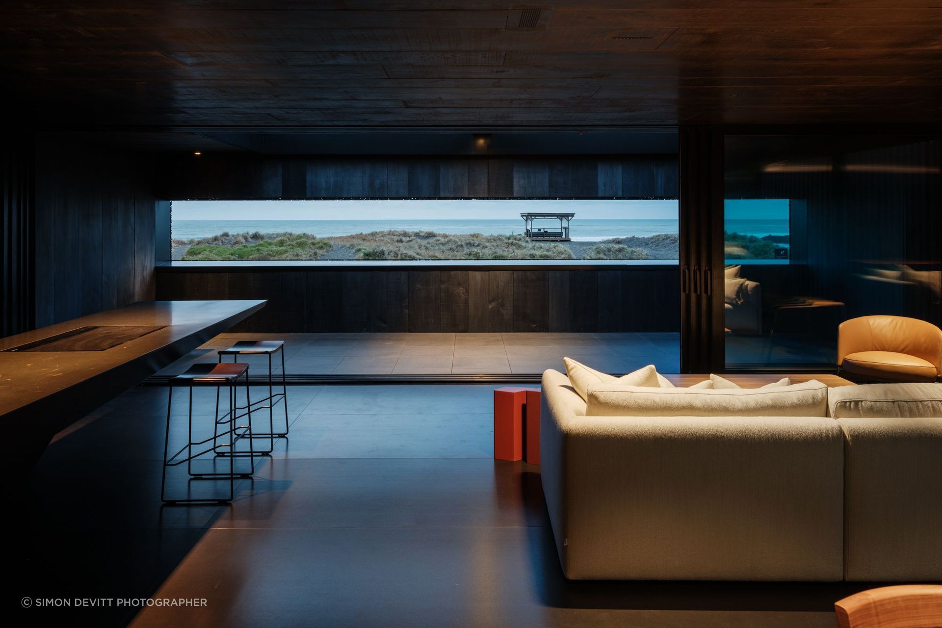 An inner reflection of the iconic black sands before it at The Bunker House in Piha, featuring VidaSpace's Consul Hand Grade Timber Flooring. | Photography: Simon Devitt Photographer