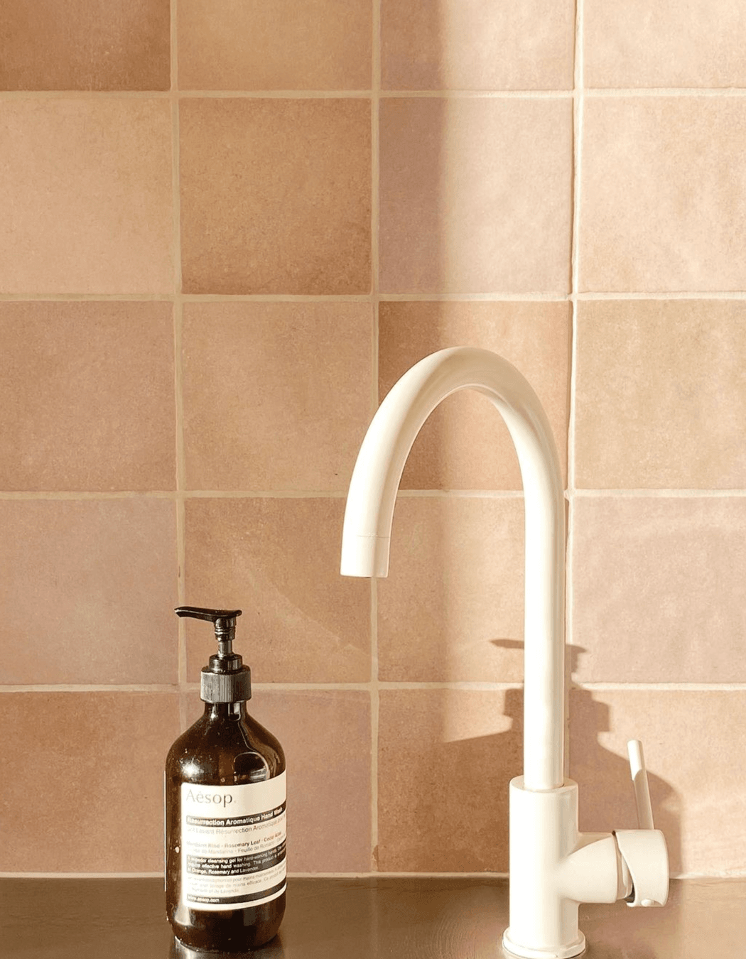 An ABI Interiors kitchen sink mixer in Almond pairs with the terracotta pink kitchen splashback.