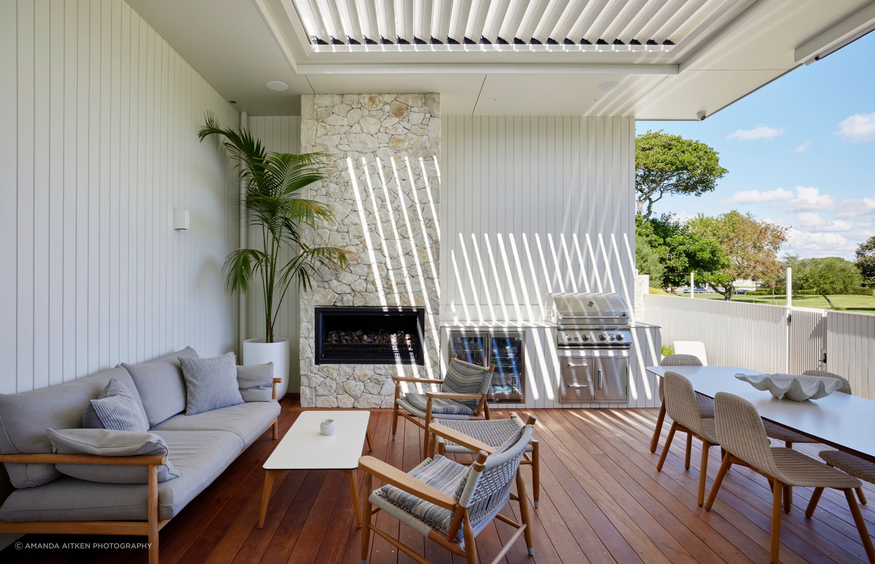 Sliding doors open the kitchen onto an outdoor dining area centred around a limestone fireplace and complete with a built-in fridge, barbecue, and seating.