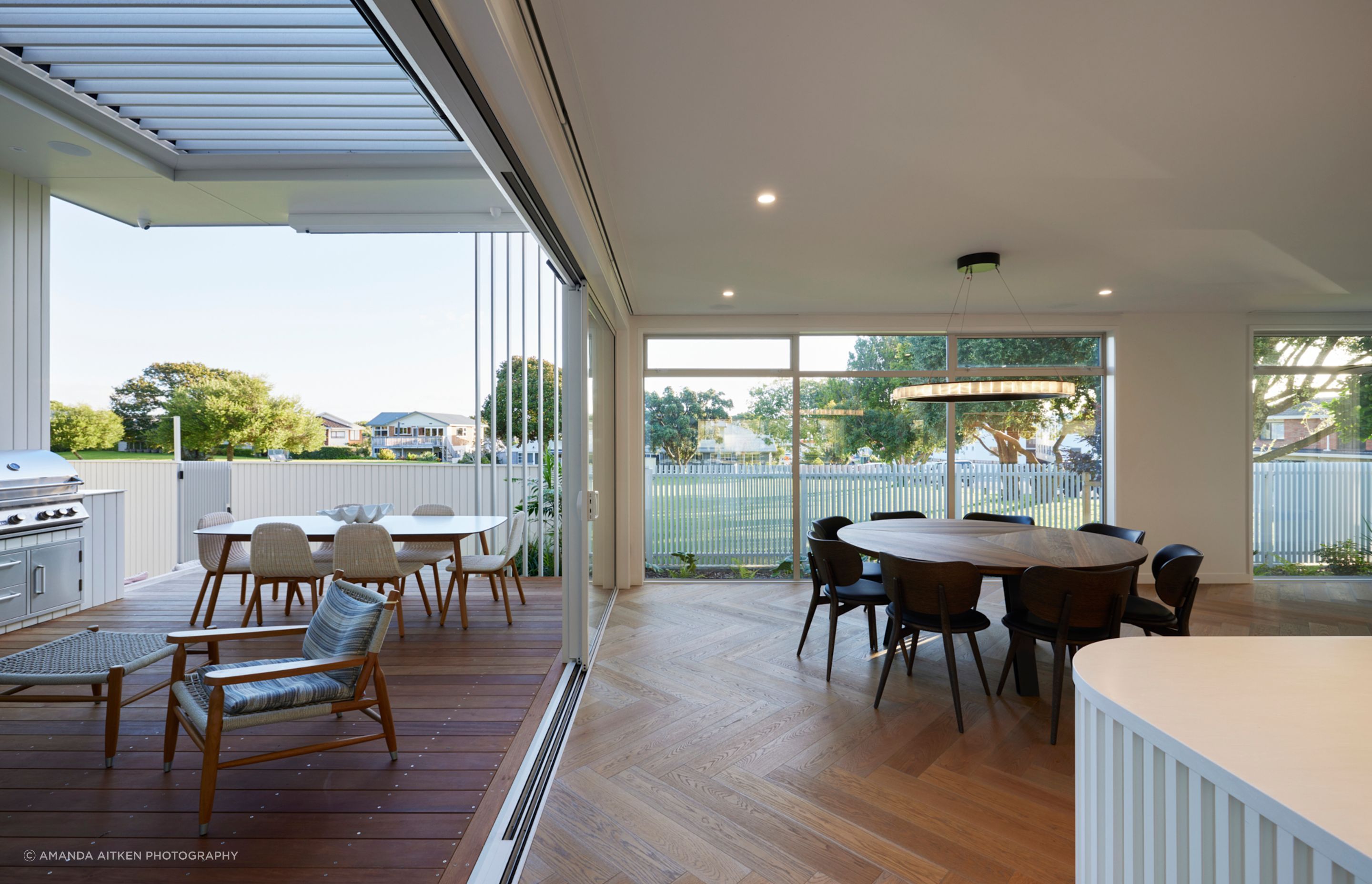 Sliding doors open up to link interior and exterior kitchen and dining areas, while swathes of glass fill the sightline with lush green space.