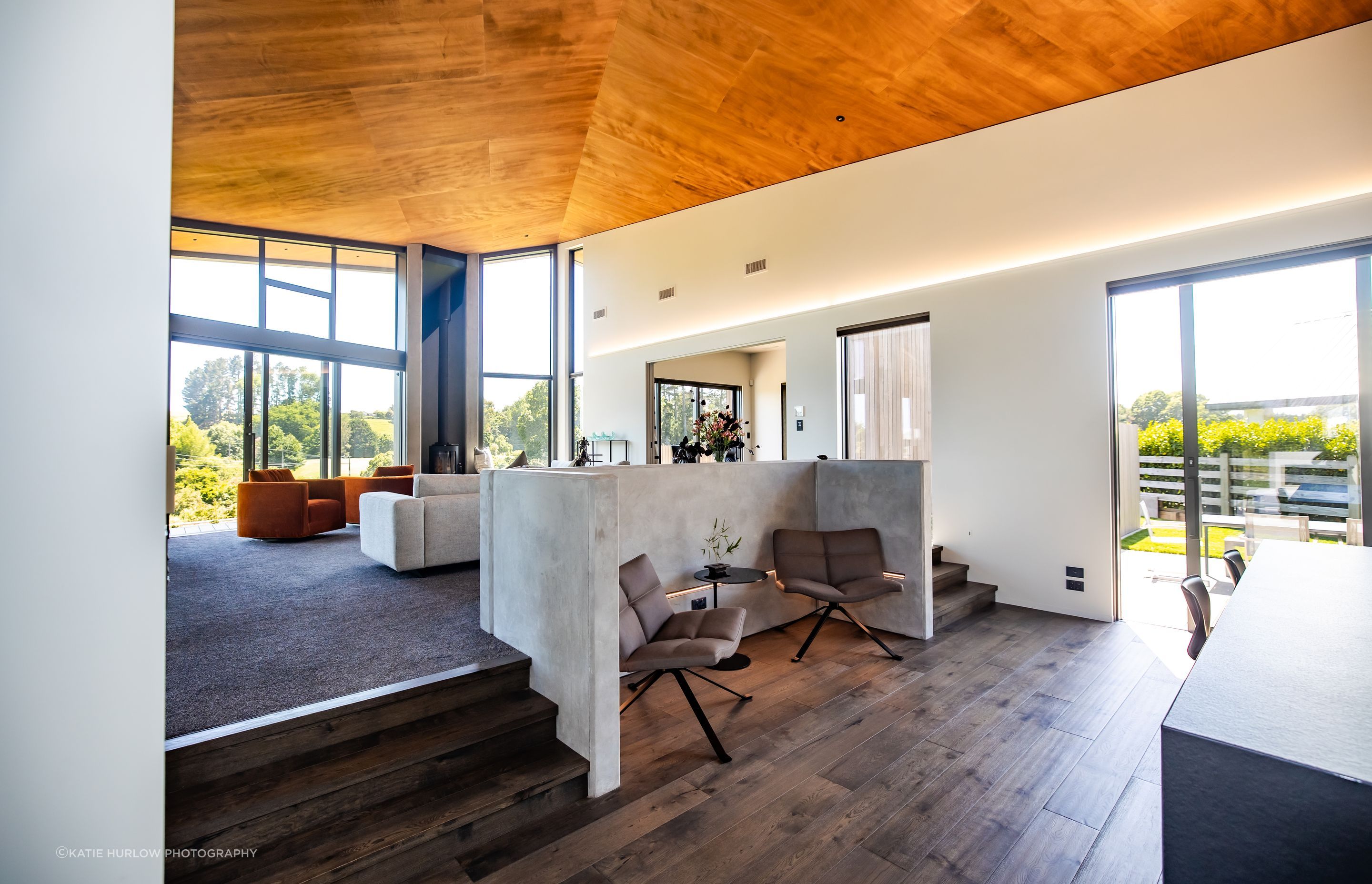 The lounge space lifts up several steps from the kitchen, creating a dynamic juxtaposition, with the angled ceiling floating over both spaces.