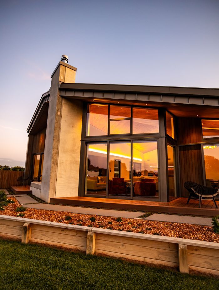The tray-style roofing tucks down over the home, juxtaposing with the concrete forms and timber decking.