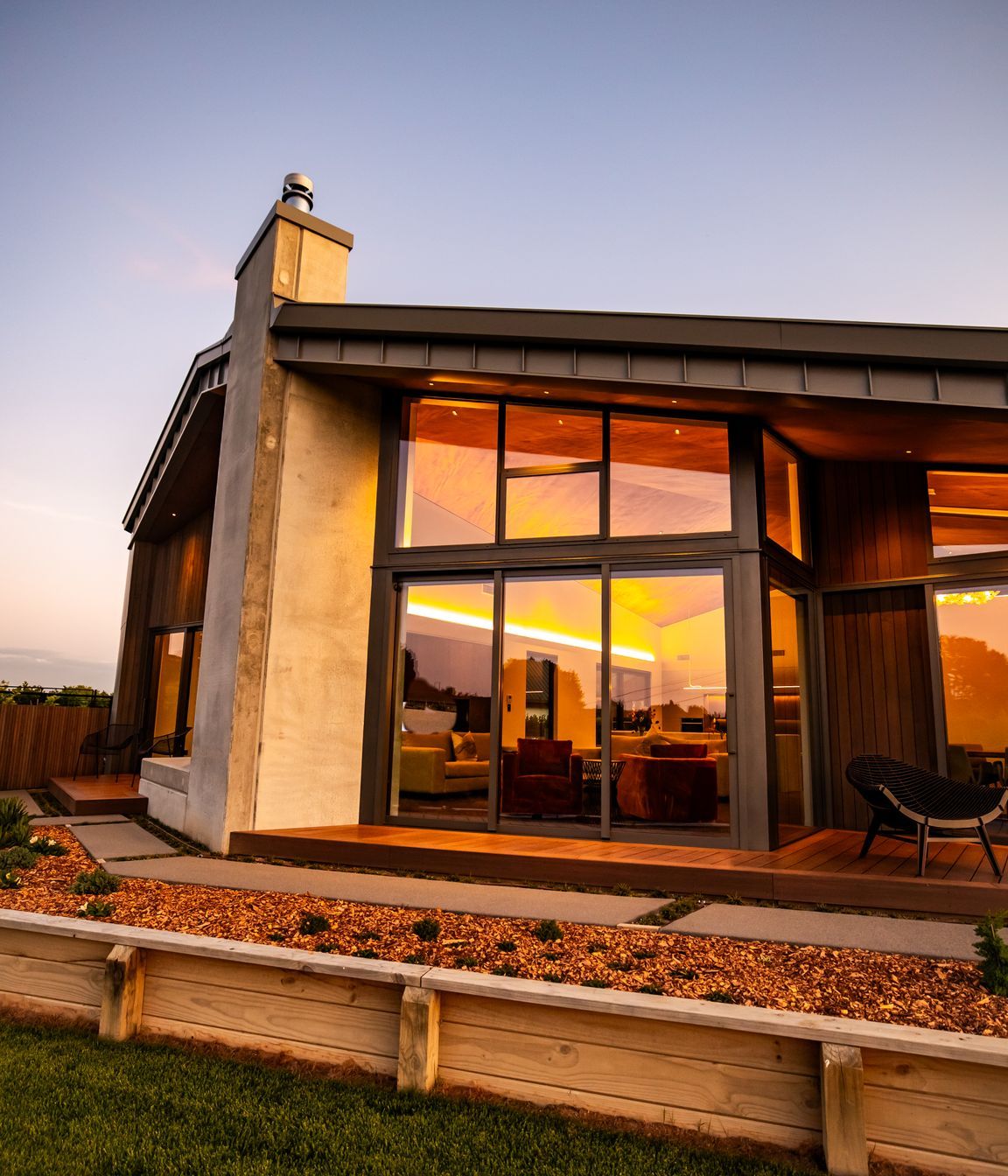 The tray-style roofing tucks down over the home, juxtaposing with the concrete forms and timber decking.