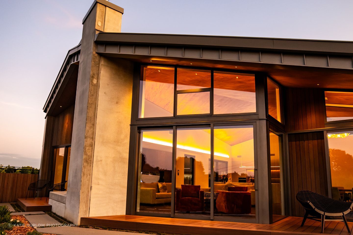The tray-style roofing tucks down over the home, juxtaposing with the concrete forms and timber decking.