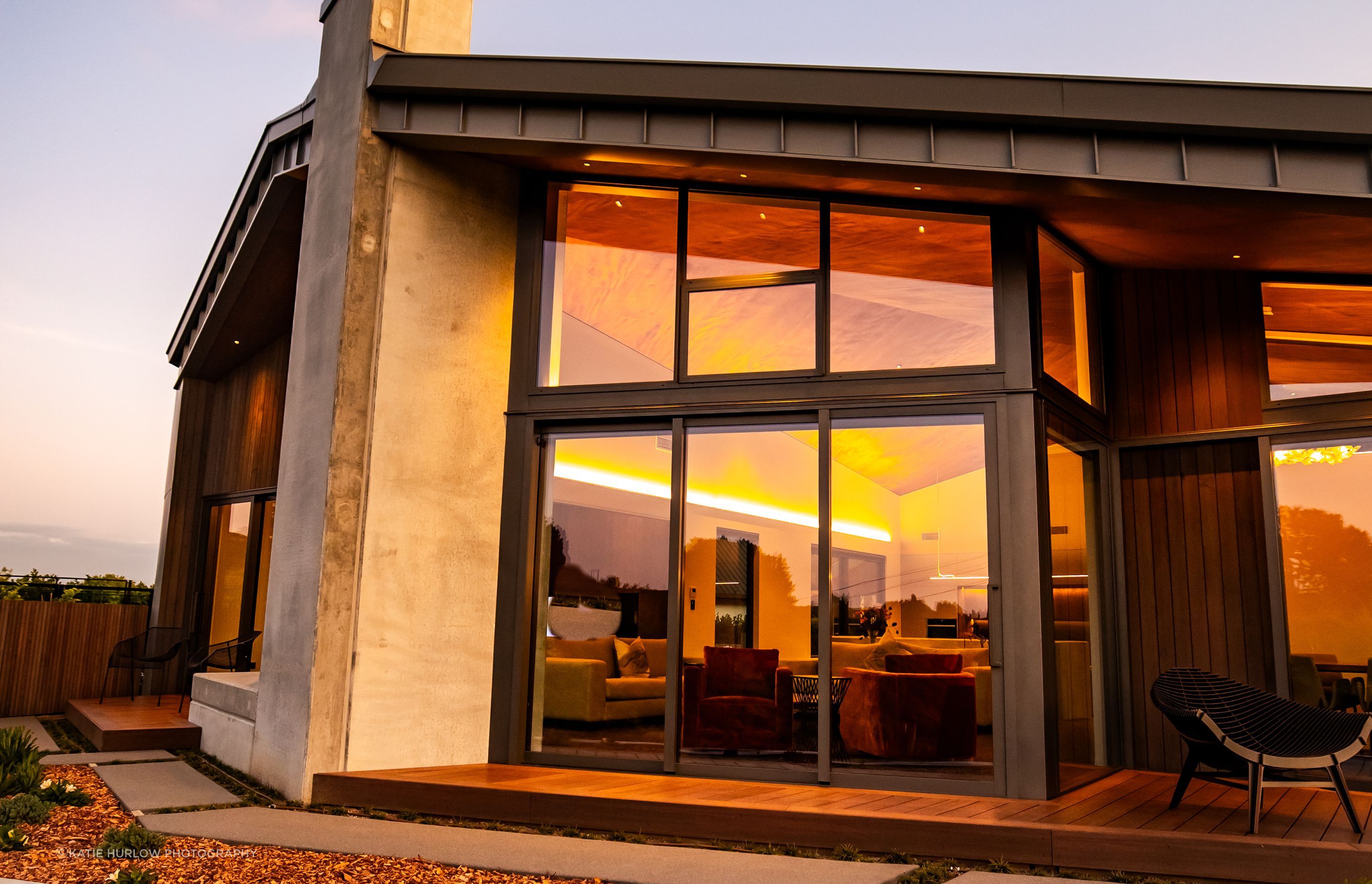 The tray-style roofing tucks down over the home, juxtaposing with the concrete forms and timber decking.