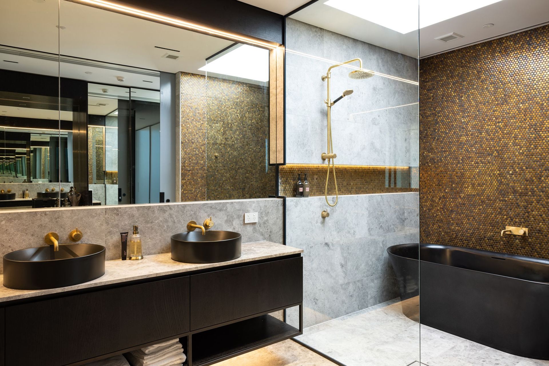 A luxurious bathroom impresses with a black freestanding bathtub, brass fittings and a copper penny round feature wall.