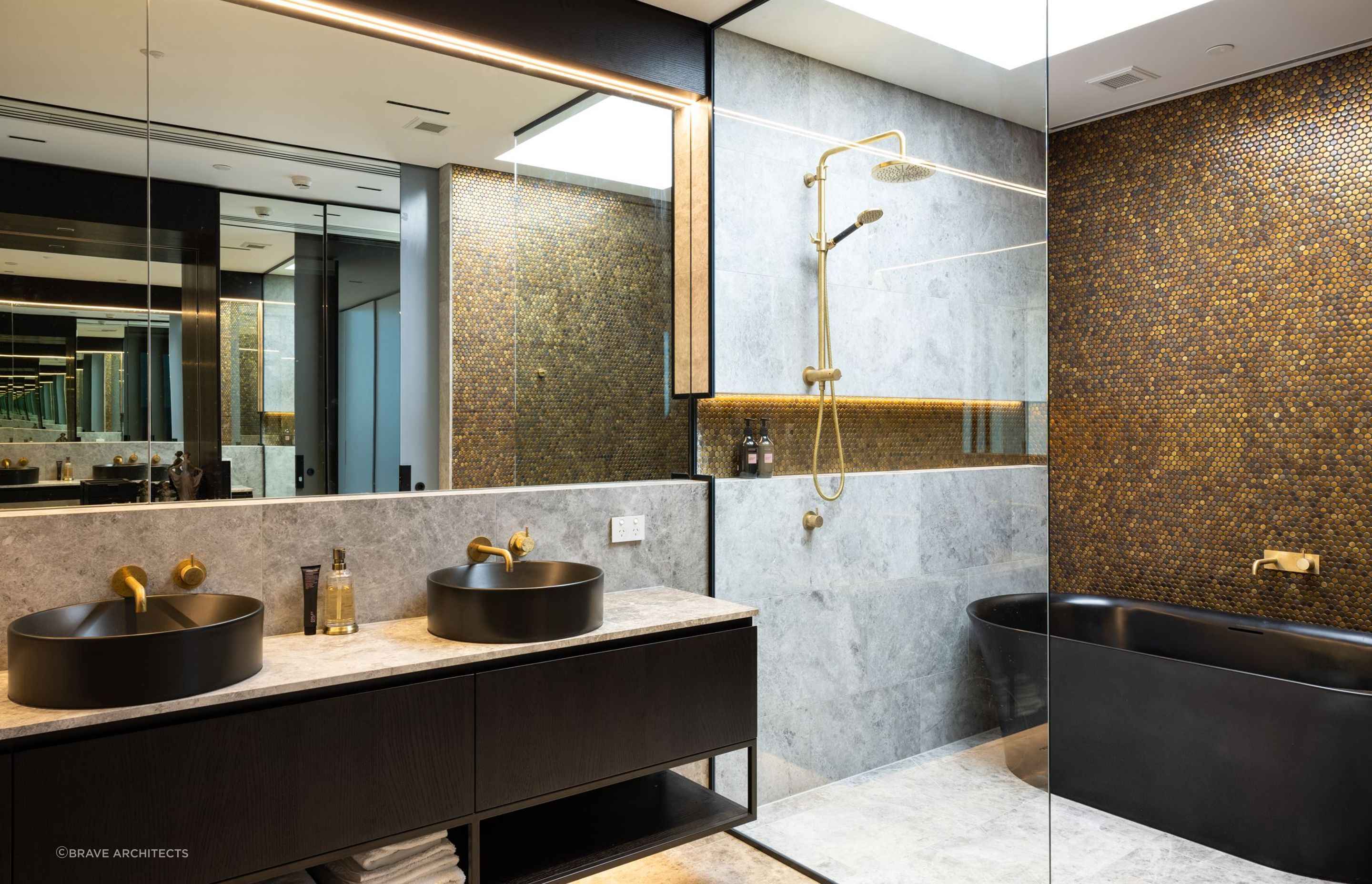 A luxurious bathroom impresses with a black freestanding bathtub, brass fittings and a copper penny round feature wall.