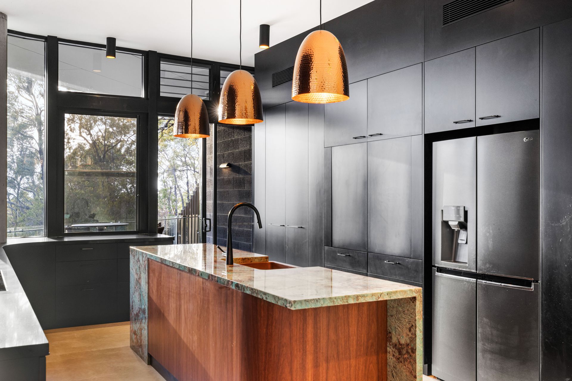 The dark cabinetry in the kitchen, contrasts against the timber veneer kitchen island and copper pendant lights.
