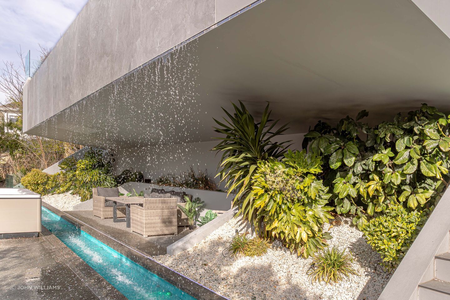 An intimate grotto is recessed behind the waterfall's downpour, complemented by lush foliage.