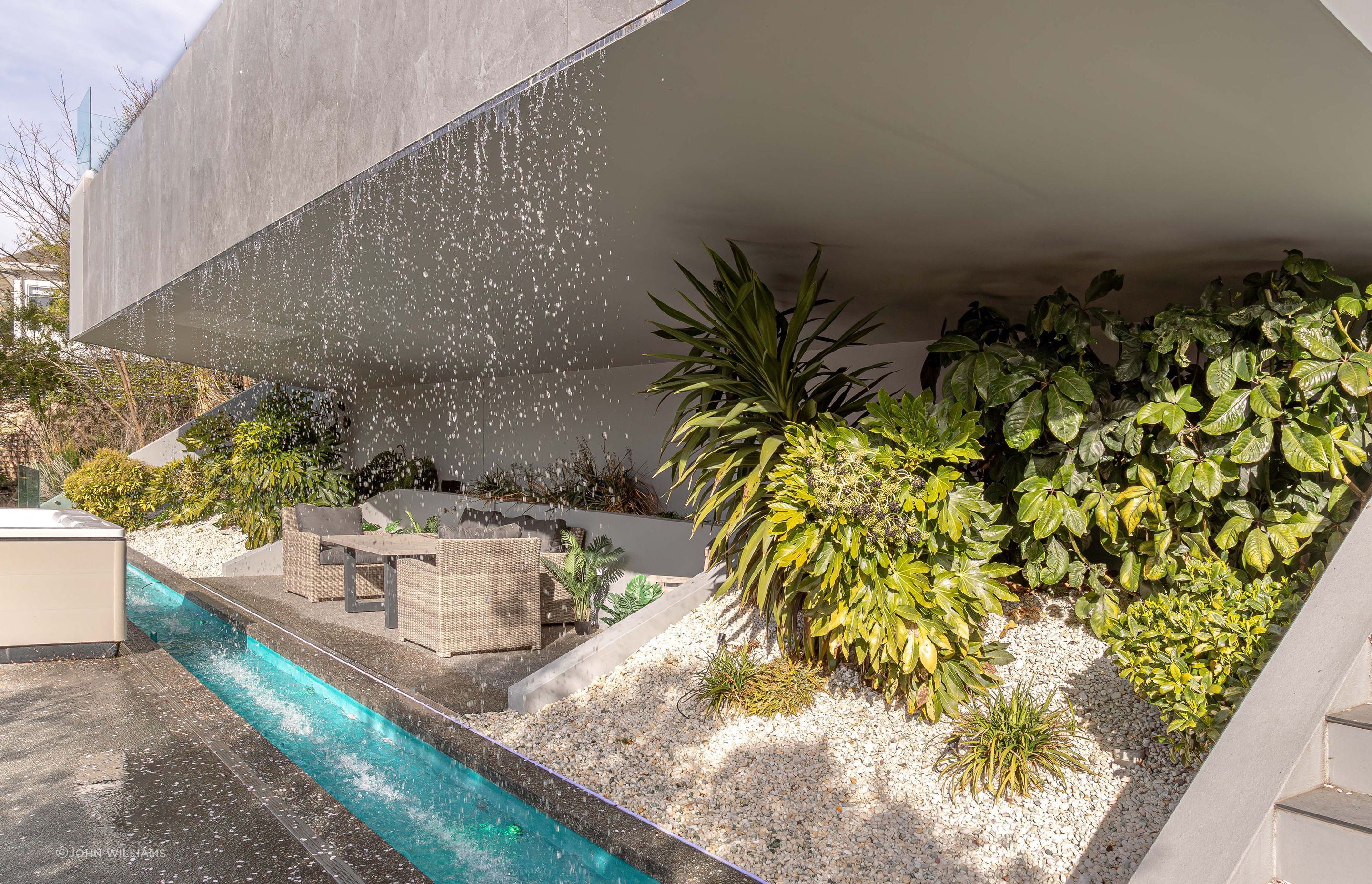 An intimate grotto is recessed behind the waterfall's downpour, complemented by lush foliage.