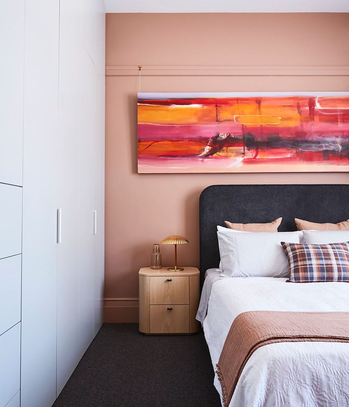 In a bedroom, a pop of pink uplifts and integrates the artwork