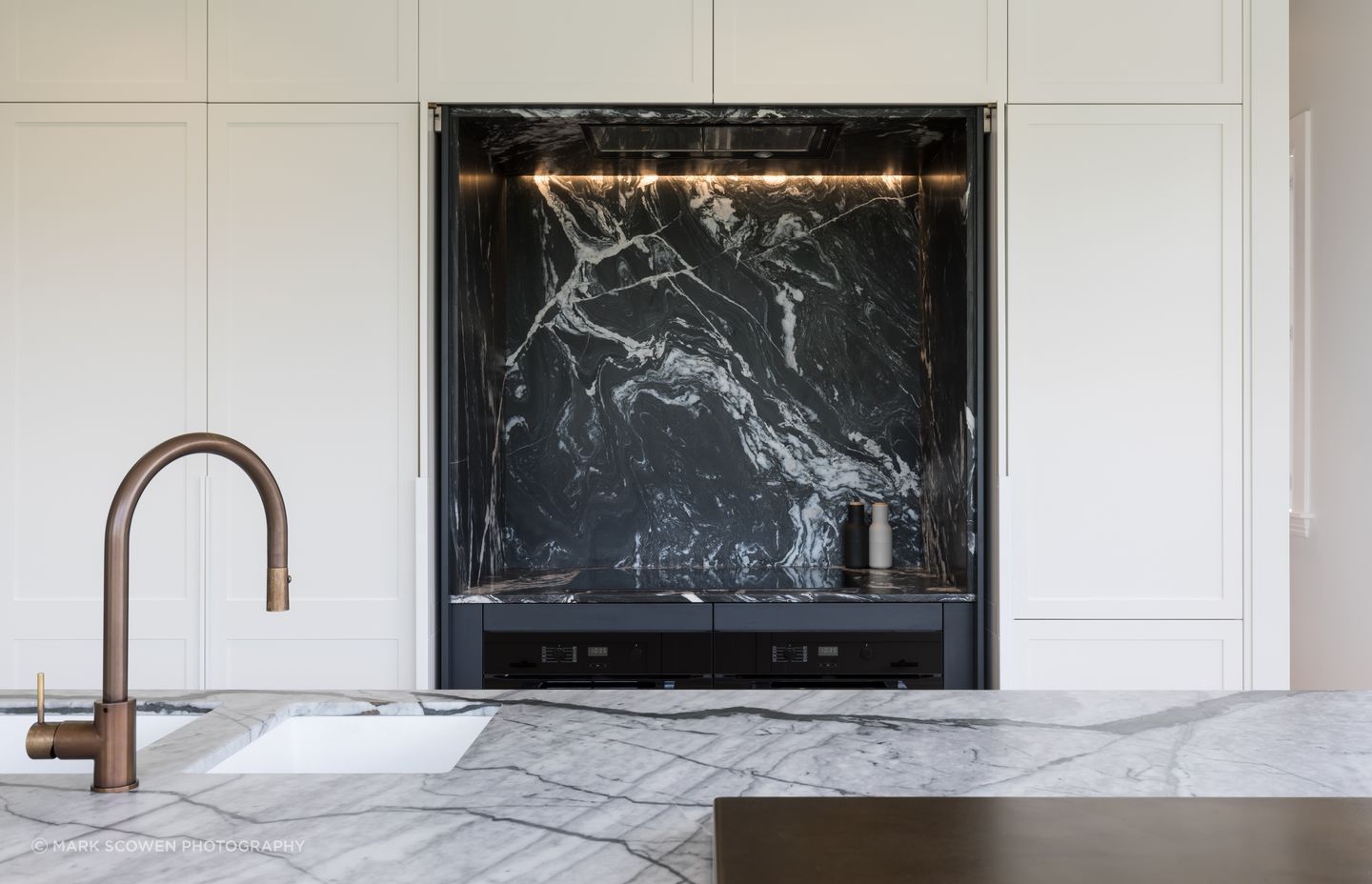 The kitchen in this Auckland family home renovation features Hawa Concepta doors by Häfele in the hob area that pivot and retract into pockets, exposing the bold dark marble counterpoint to the light marble of the island.