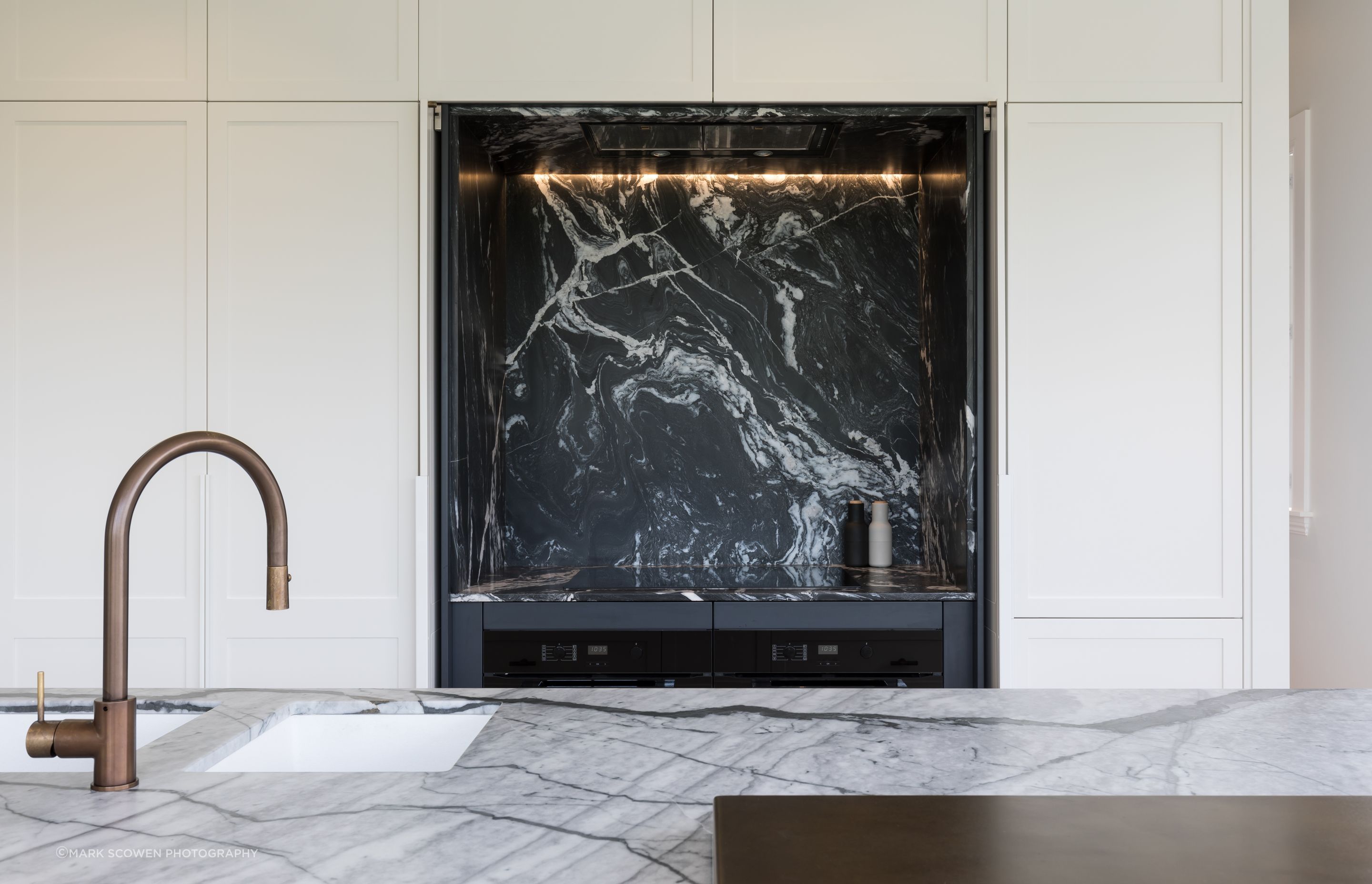 The kitchen in this Auckland family home renovation features Hawa Concepta doors by Häfele in the hob area that pivot and retract into pockets, exposing the bold dark marble counterpoint to the light marble of the island.