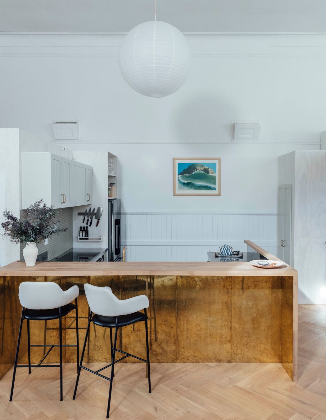 The kitchen features a timber breakfast bar and brass details. 