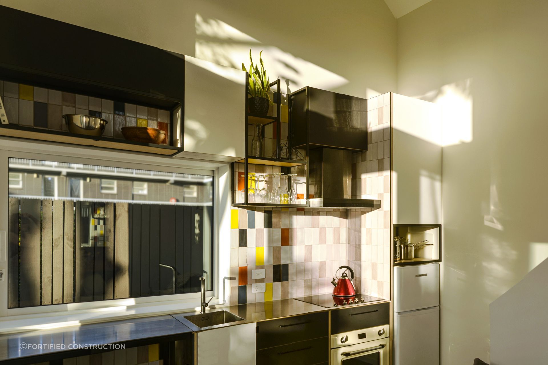 Coloured tiles accent the kitchen, juxtaposed with the monochrome cabinets, giving the room a pop of personality.