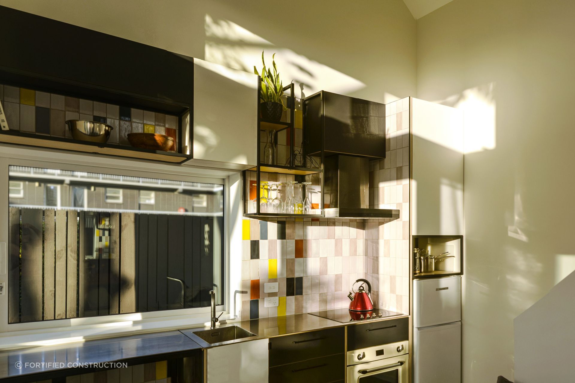 Coloured tiles accent the kitchen, juxtaposed with the monochrome cabinets, giving the room a pop of personality.