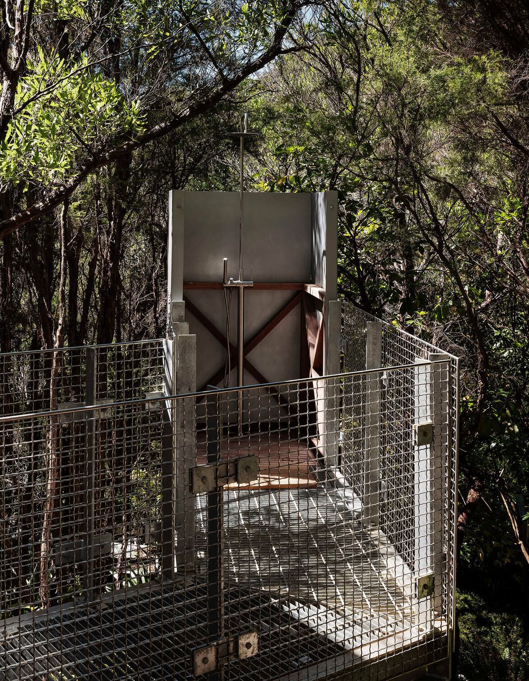 A grated metal walkway meets a shower deep in the forest.