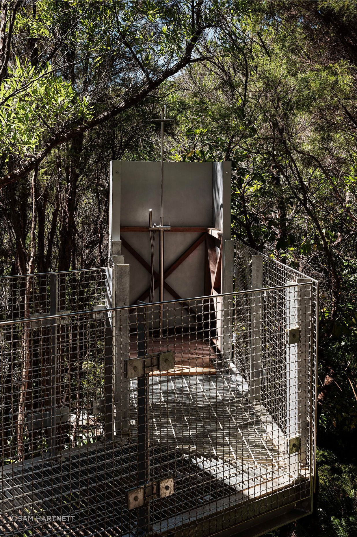 A grated metal walkway meets a shower deep in the forest.