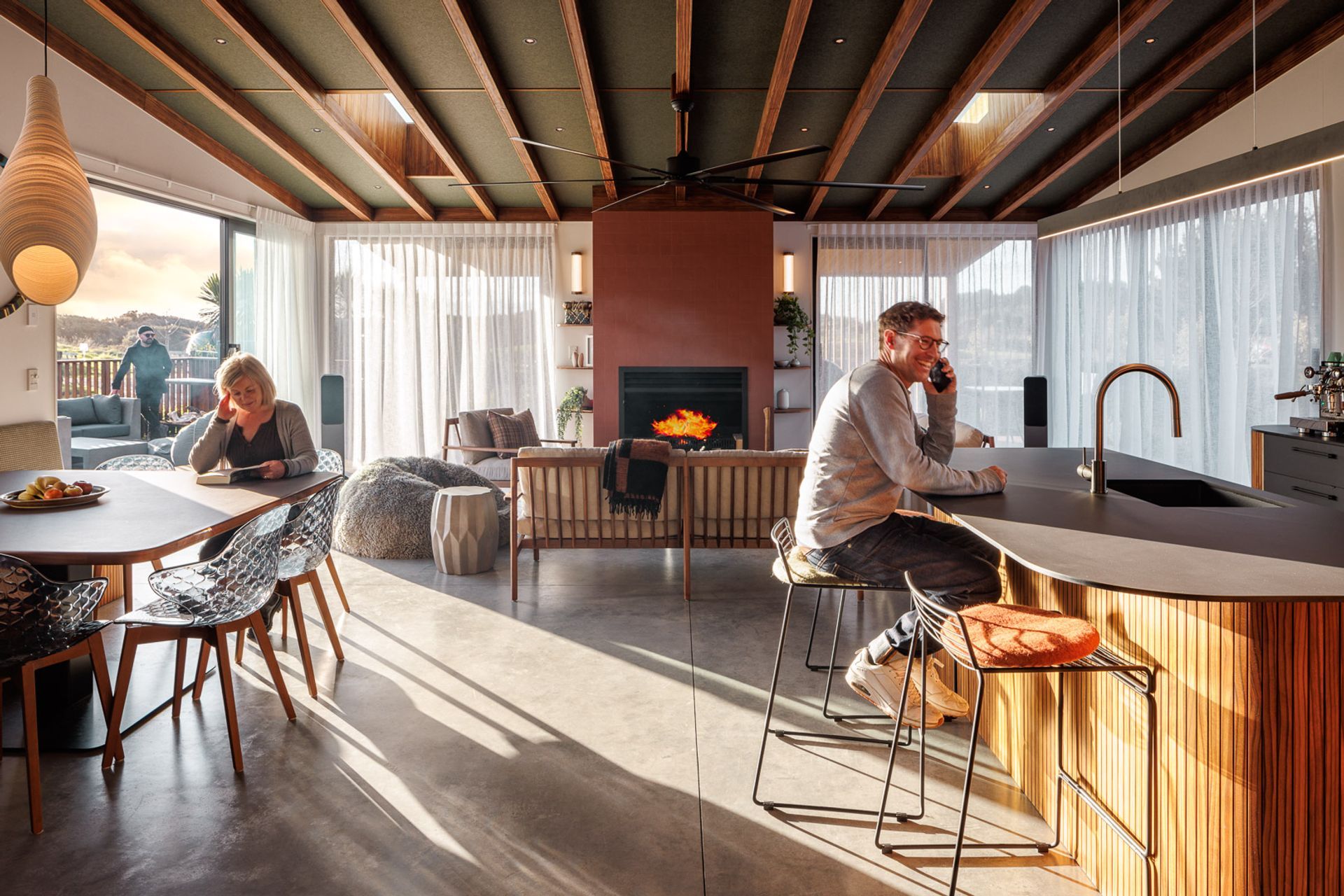 Nestled between outdoor living spaces shielded by carefully placed vertical timber battens, the open-plan kitchen, dining, and living zone fosters community with high-vaulted ceilings.